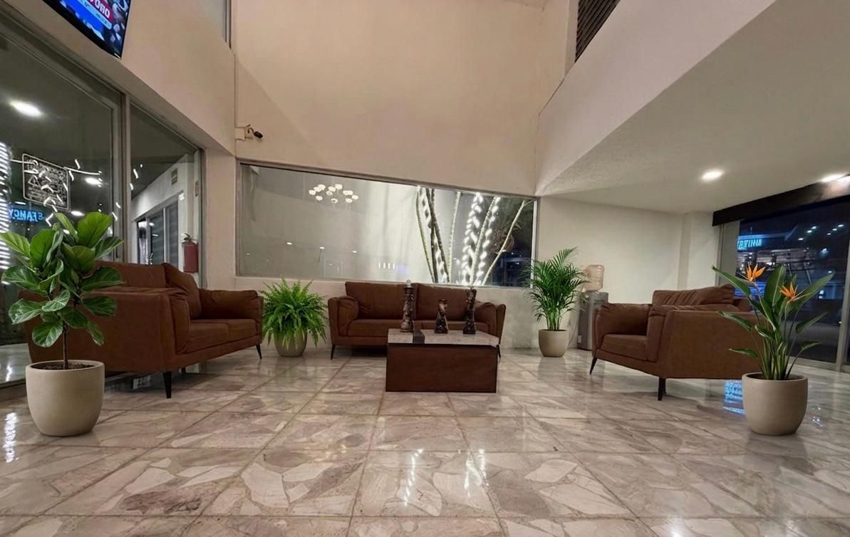 Amplio vestíbulo de hotel con sofás marrones, suelo de mármol, plantas en macetas y una iluminación moderna y brillante.