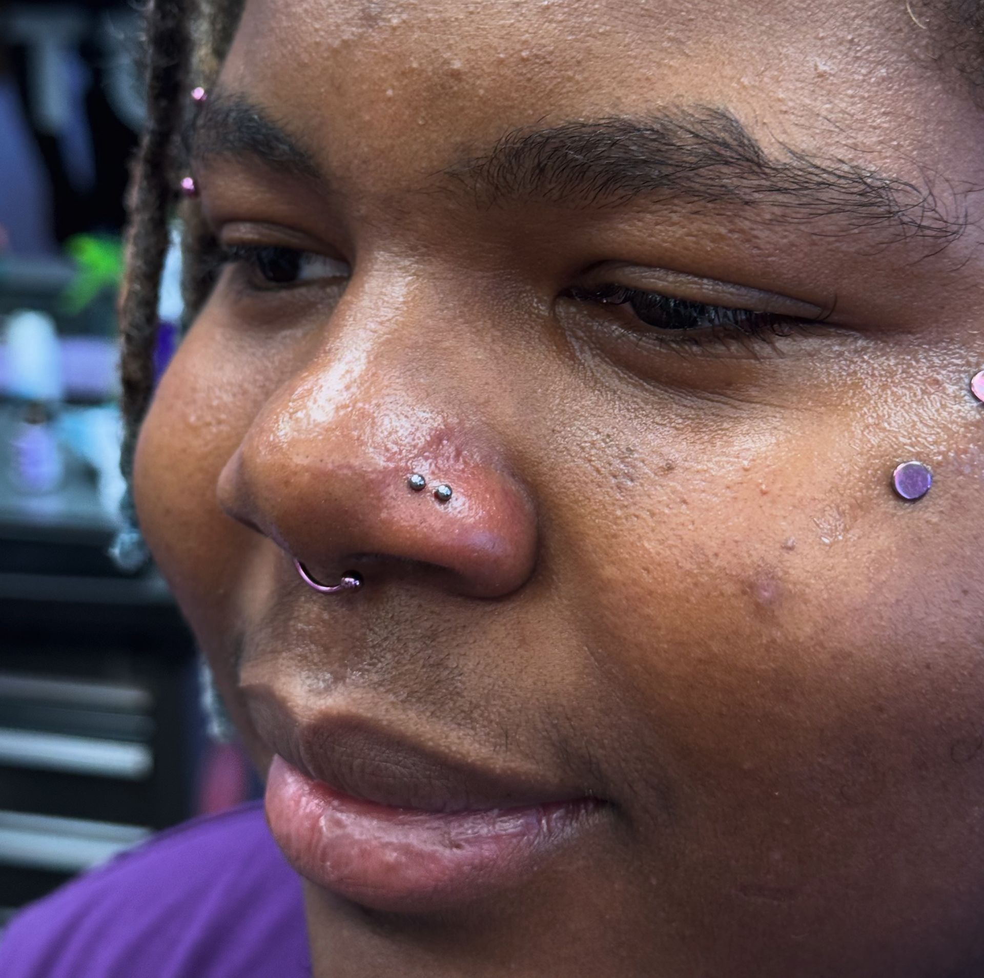 Close-up of a person’s face with a nose ring and facial piercings in a salon setting
