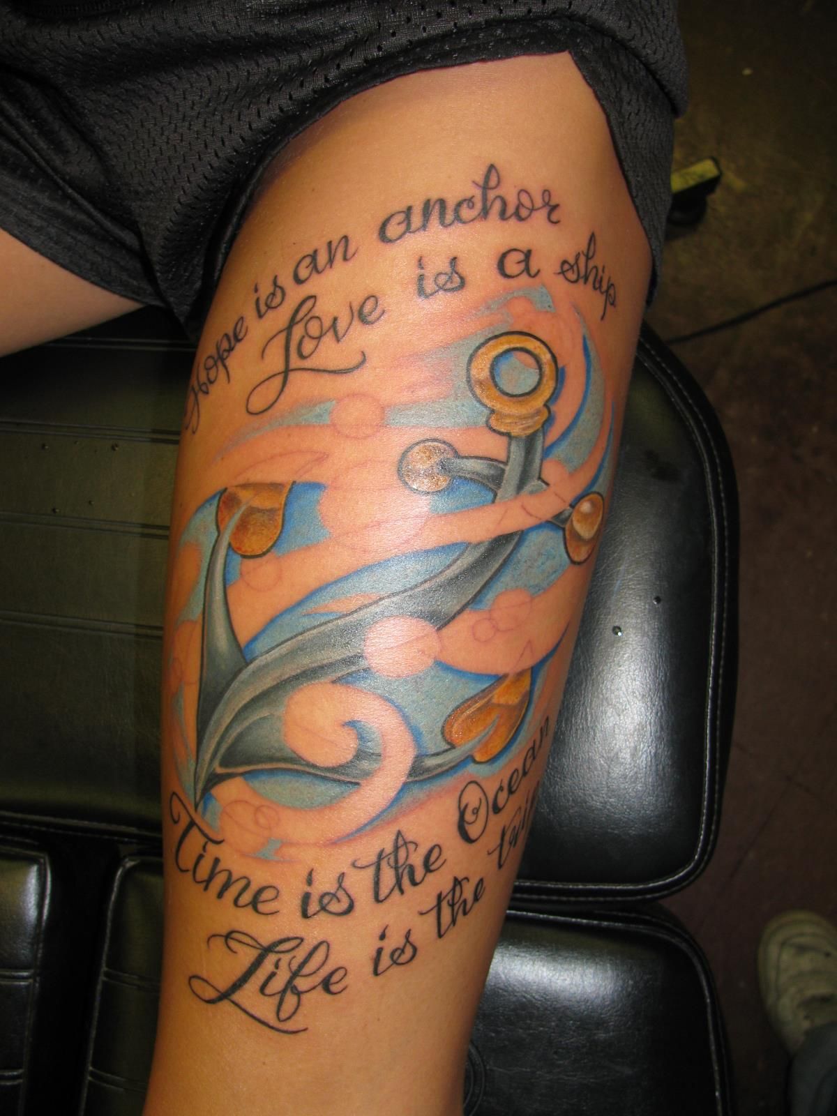 Close-up of a colorful anchor tattoo with cursive text on a person’s upper arm