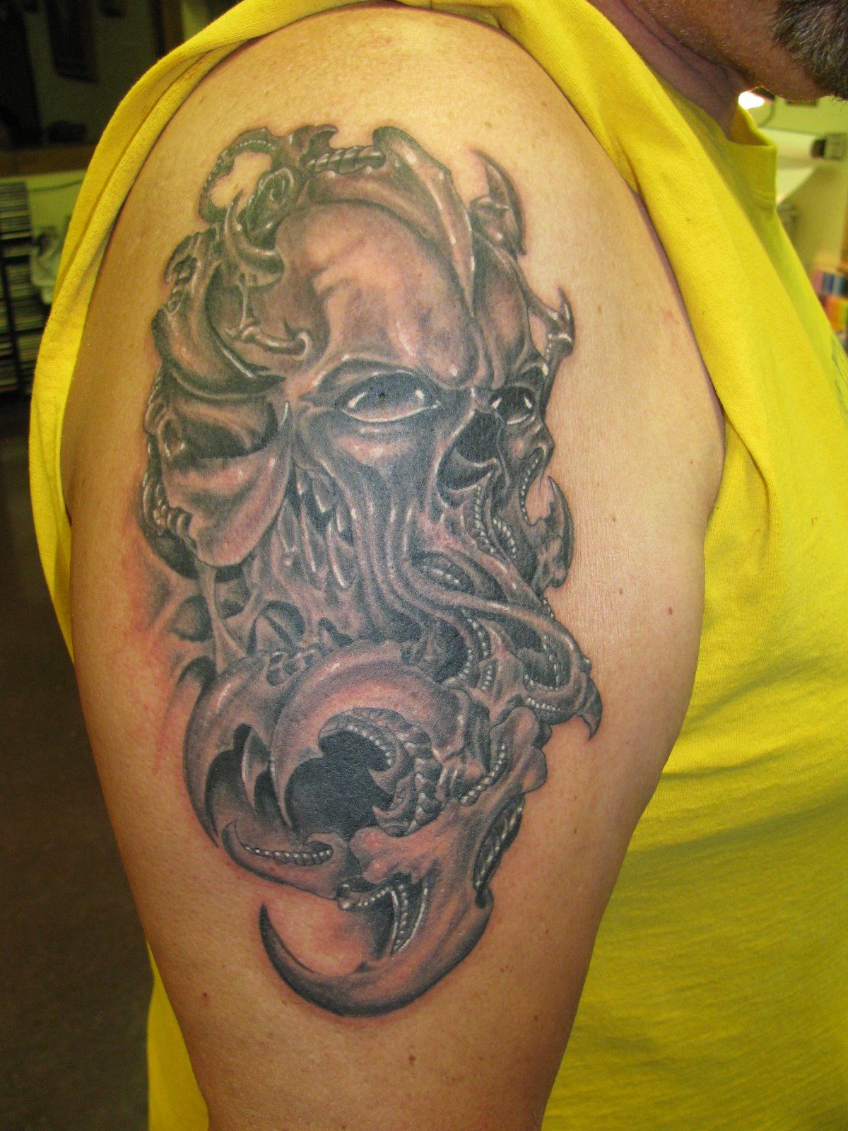 Close-up of a black and gray skull tattoo on a person’s upper arm, wearing a yellow shirt