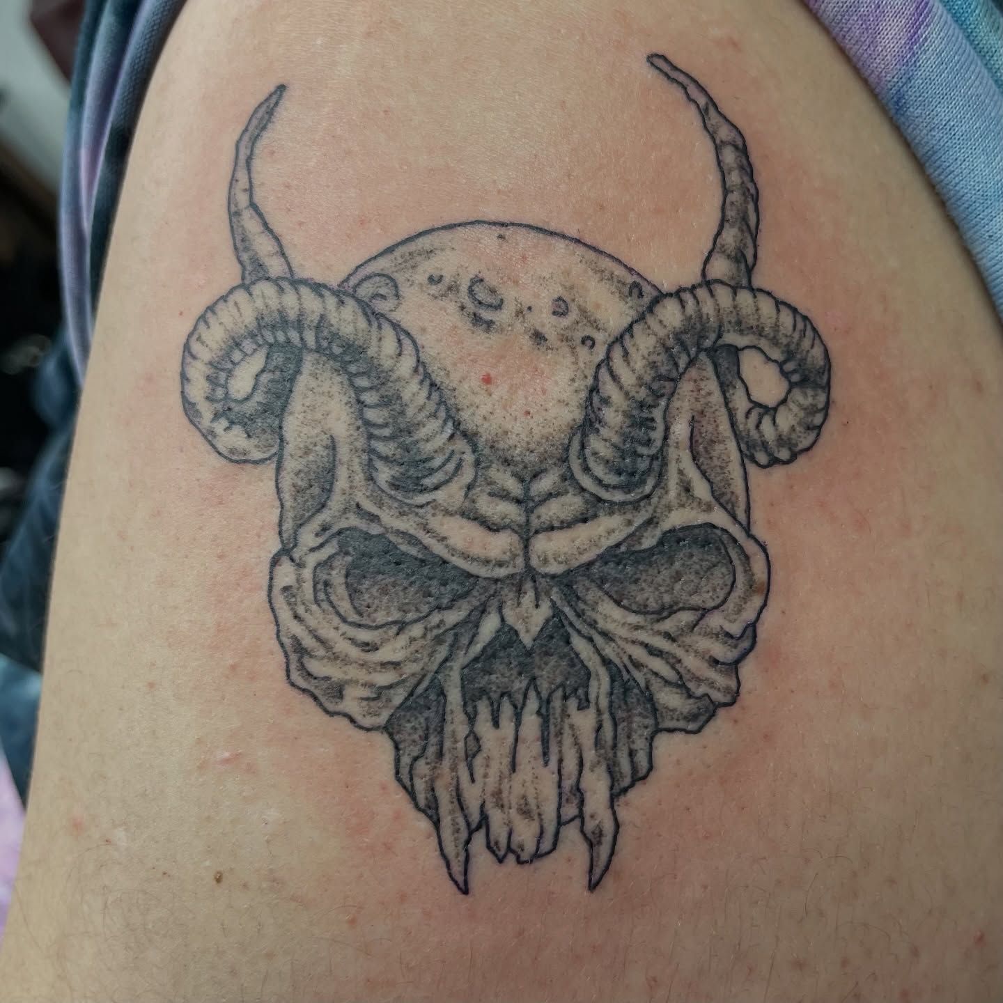 Black horned skull tattoo on skin, with curled horns and a snarling mouth