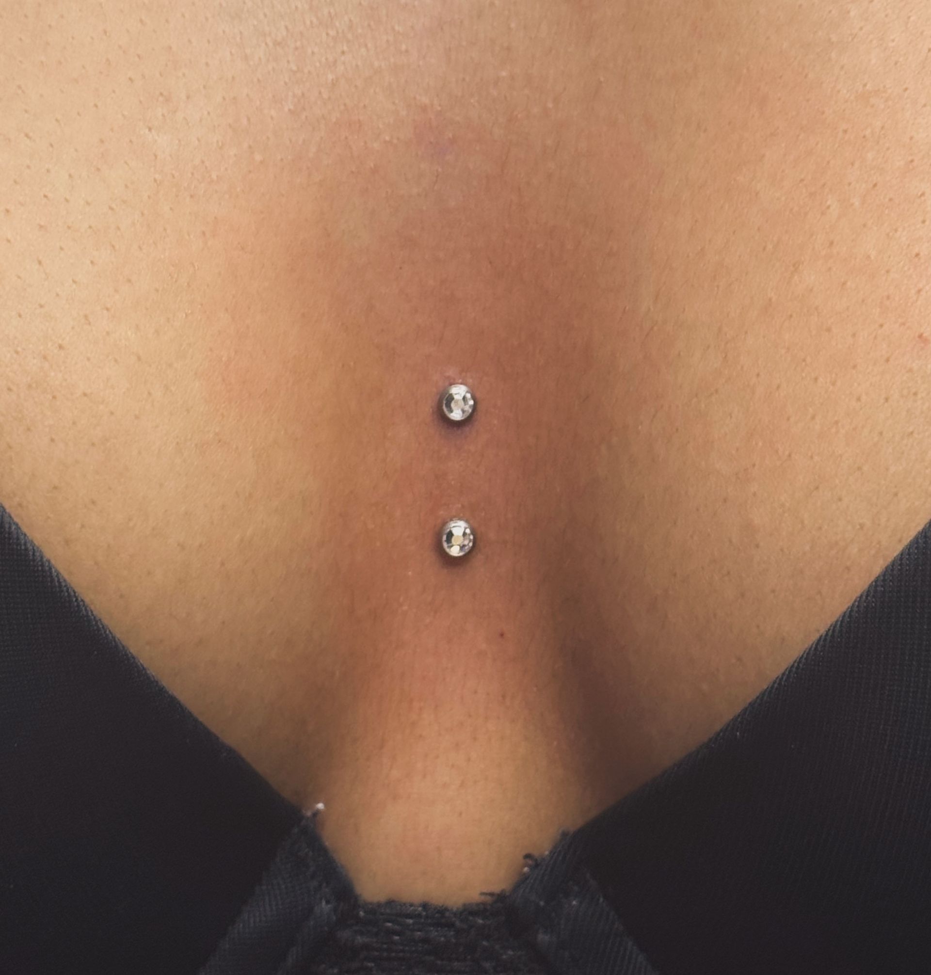 Close-up of a person's lower back with a double dermal piercing above a black top