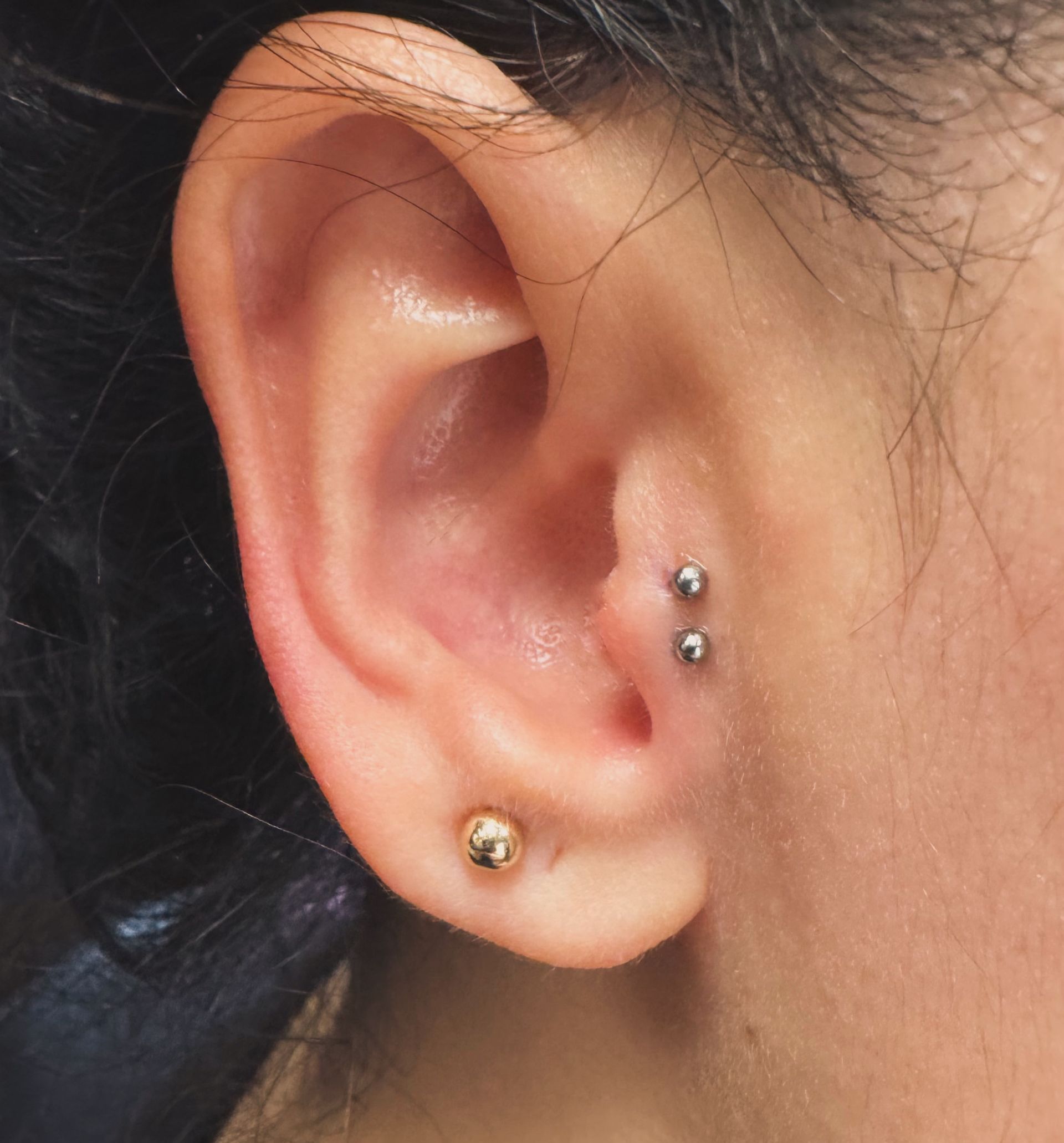 Close-up of an ear with two silver studs in the upper lobe and a gold stud in the lower lobe