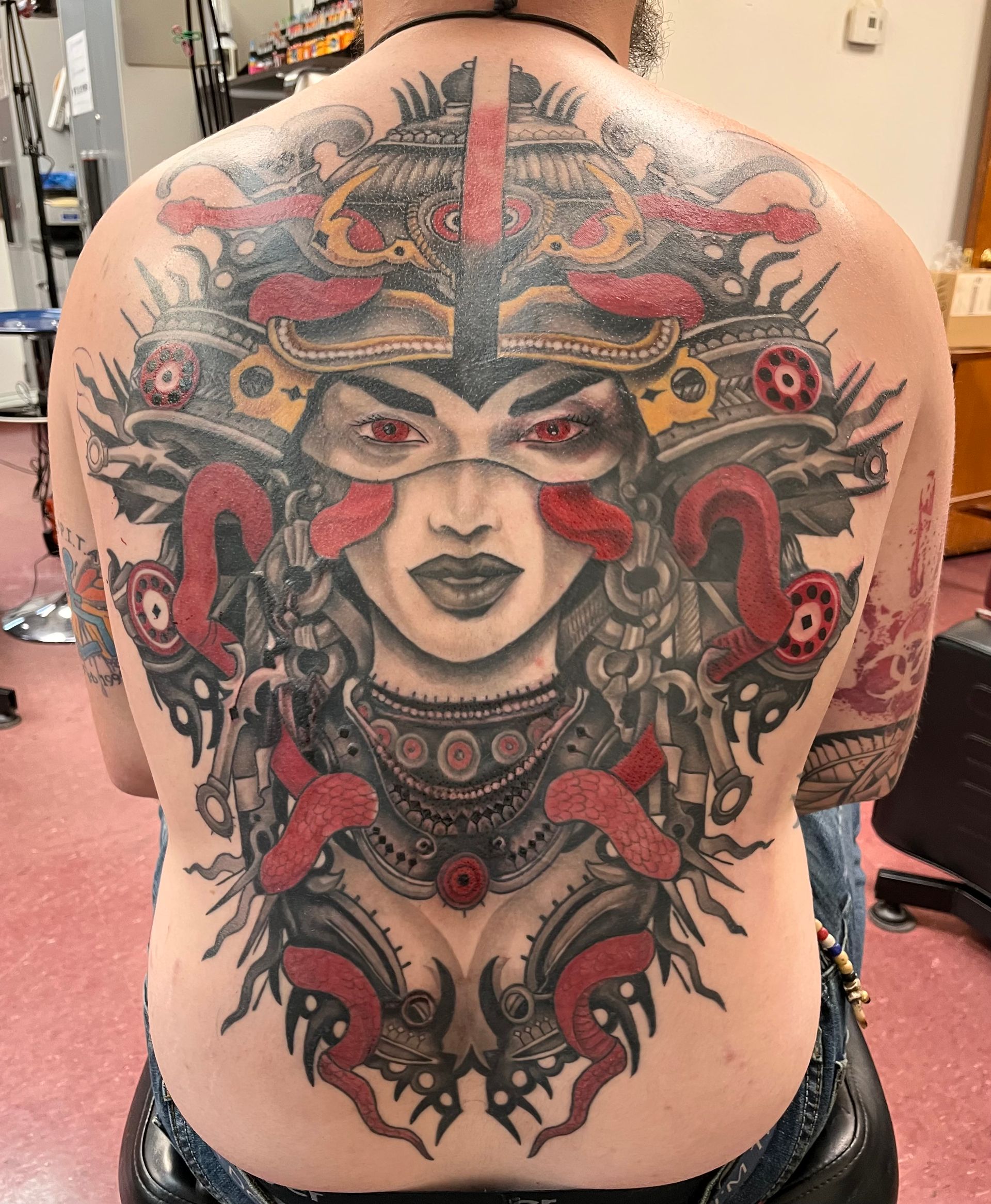 Large colorful back tattoo of a stylized face with red and black ornamental details on a person’s back