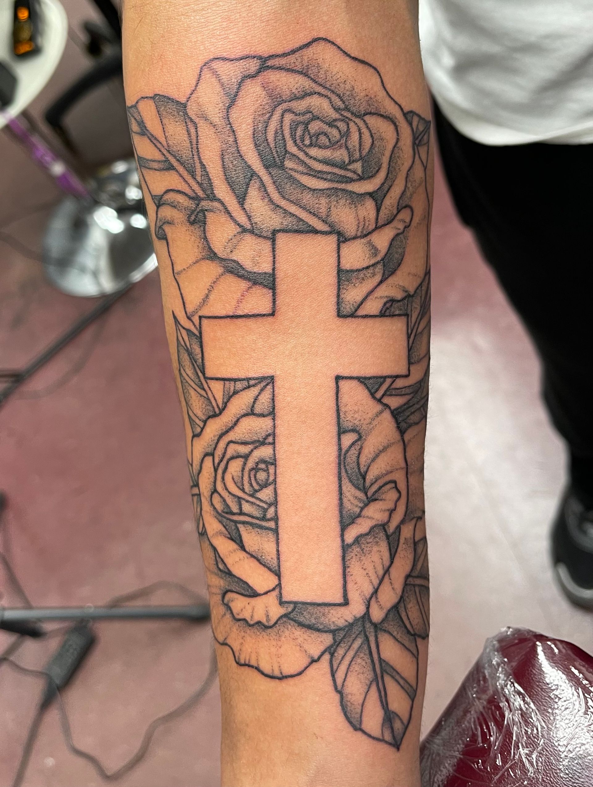 Forearm tattoo of a cross over roses, outlined in black ink on skin