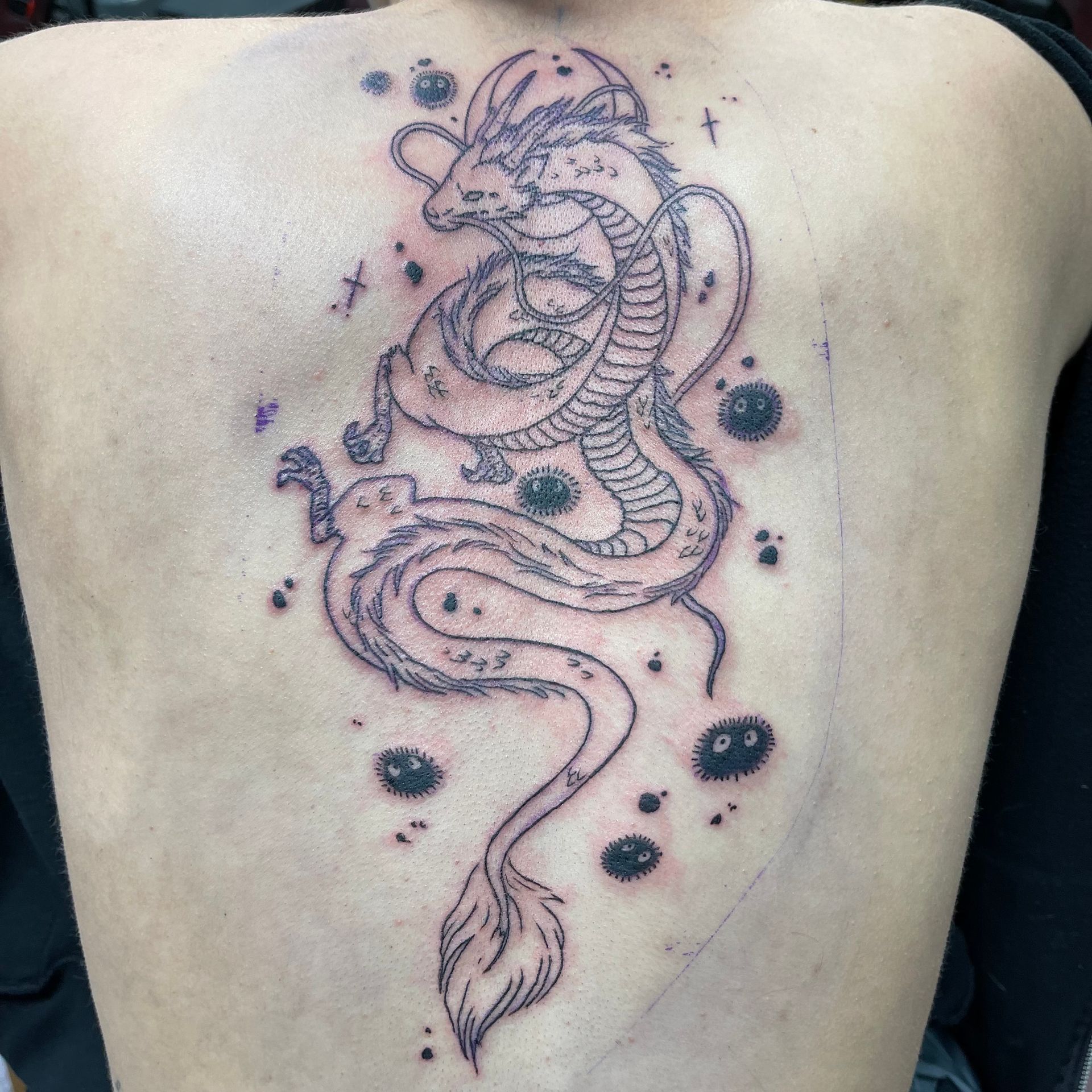Black and gray dragon tattoo coiled on a torso, with a long tail and scattered ink dots
