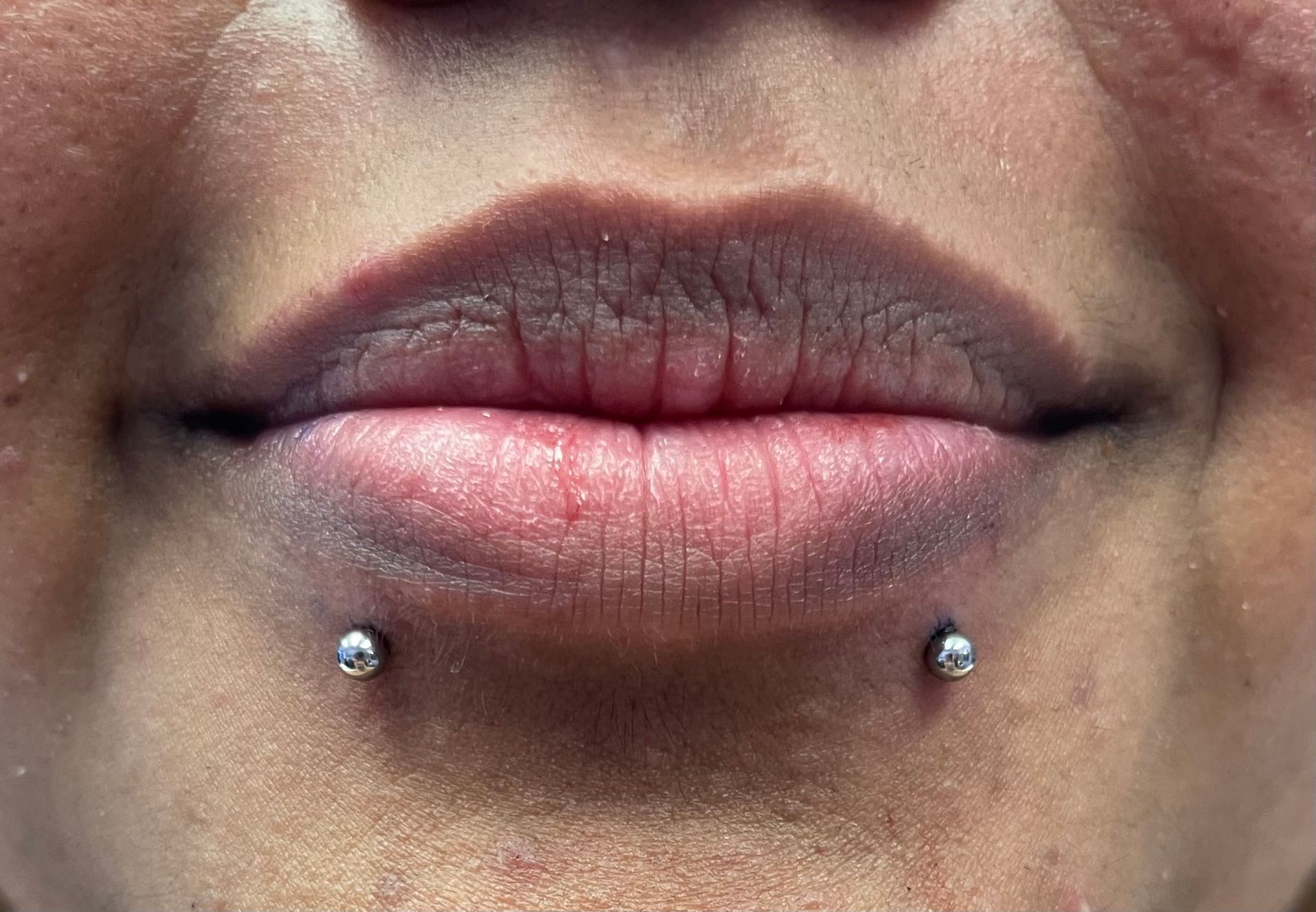 Close-up of lips with a vertical labret piercing and two silver studs below the lower lip