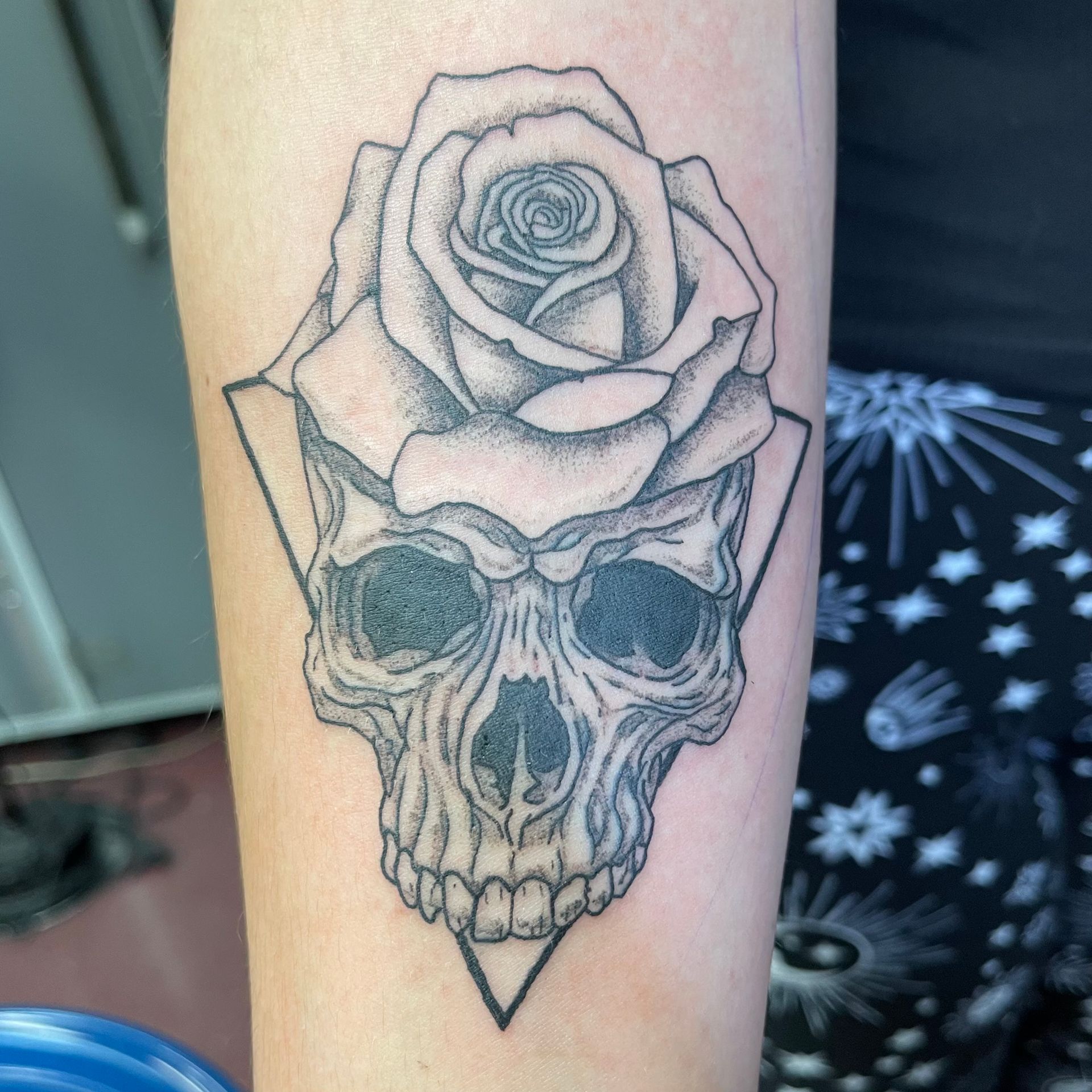 Black-and-gray skull tattoo with a rose growing from the top on a forearm.