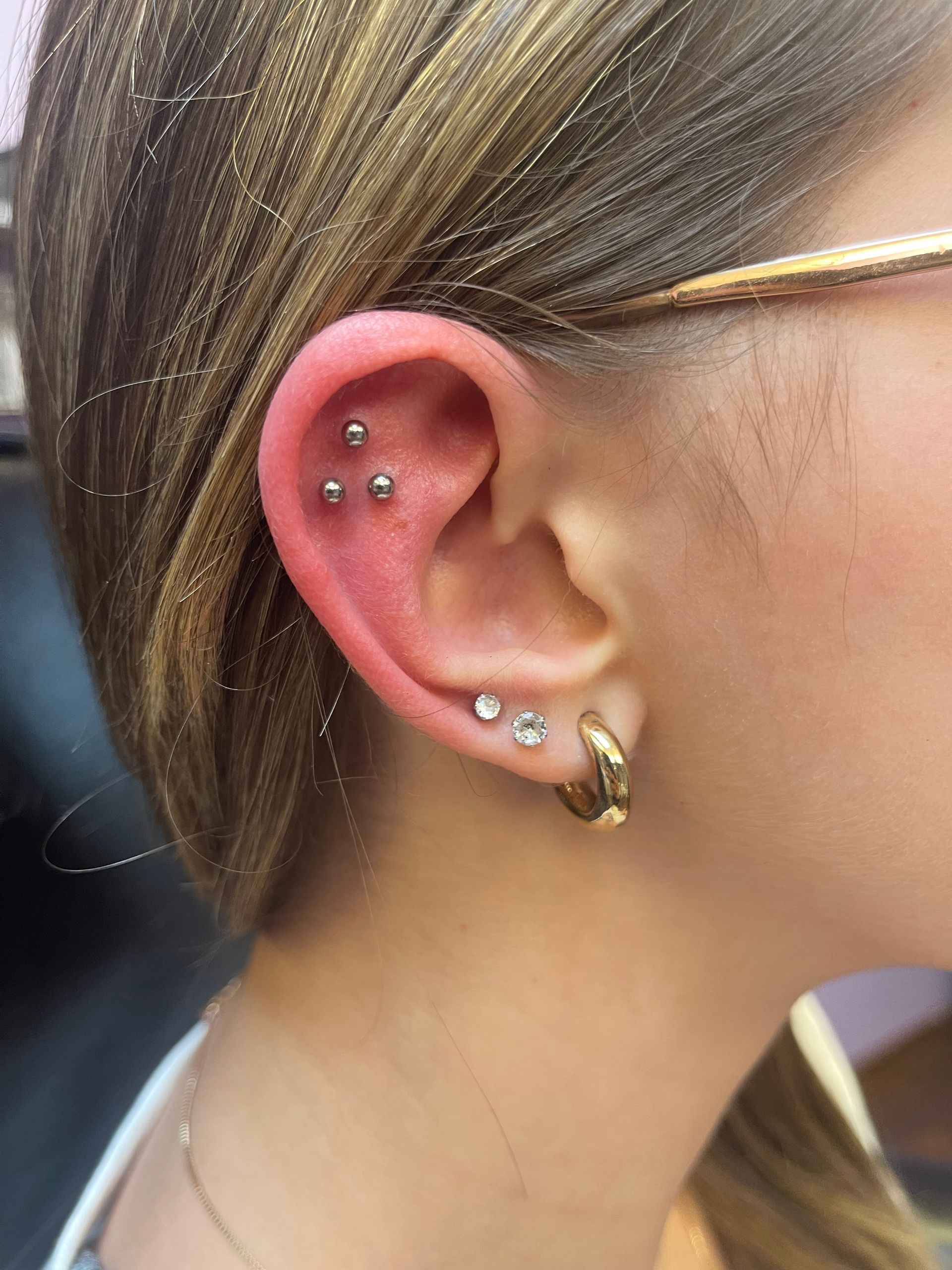 Close-up of an ear with multiple piercings and silver jewelry, hair tucked behind it