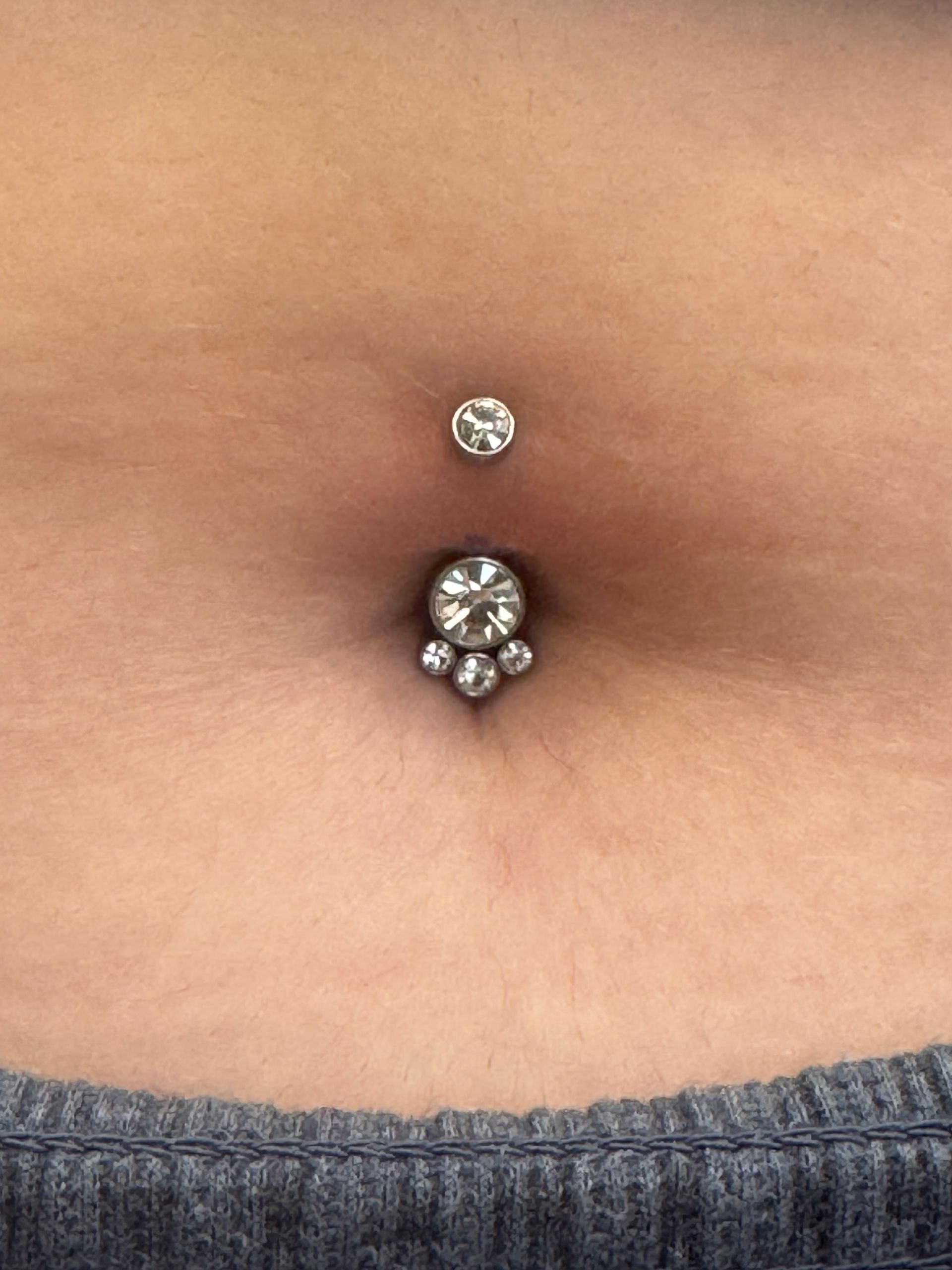 Close-up of a navel piercing with silver jewelry on bare skin above denim waistband