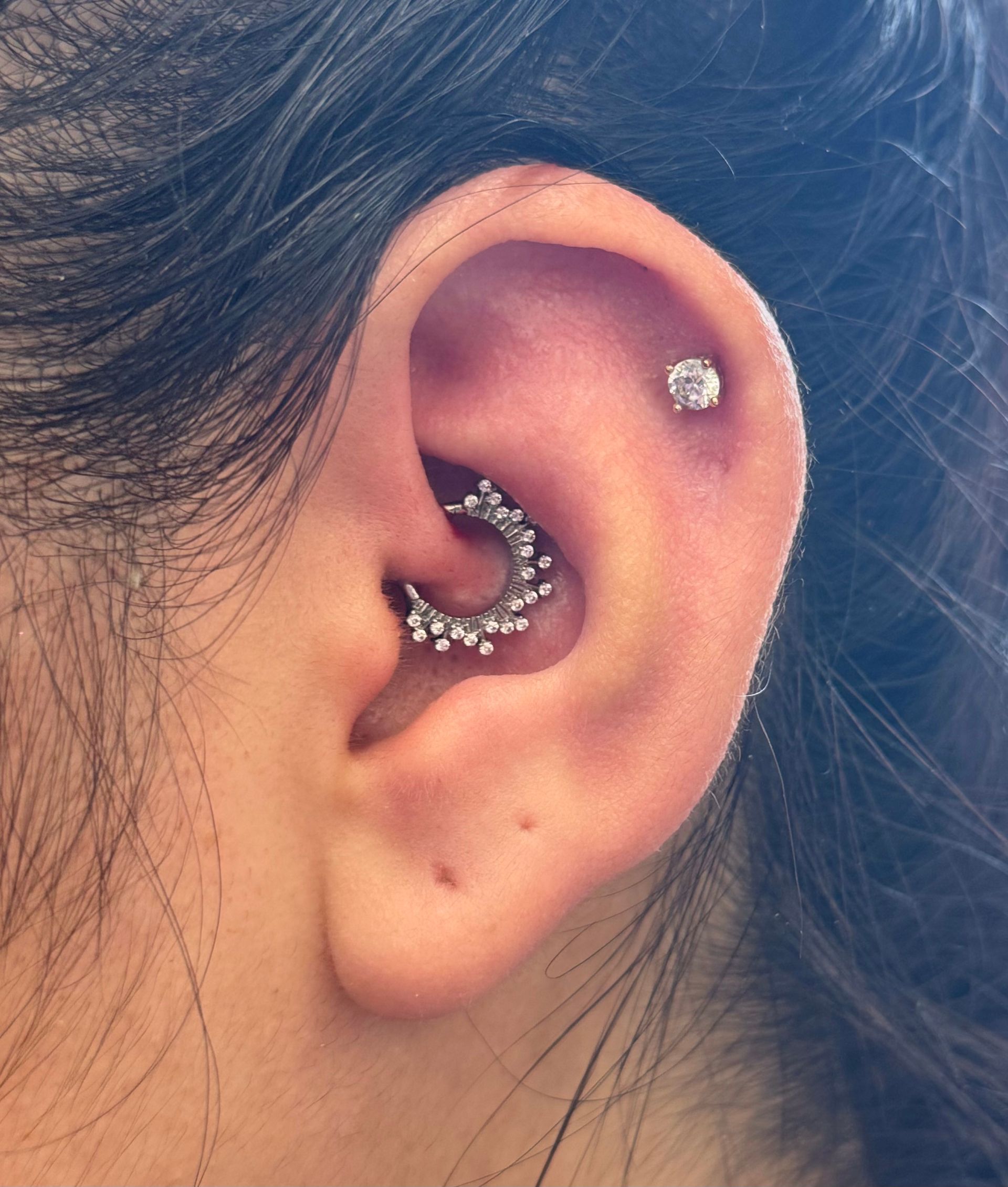 Close-up of an ear with multiple silver hoop and stud piercings.