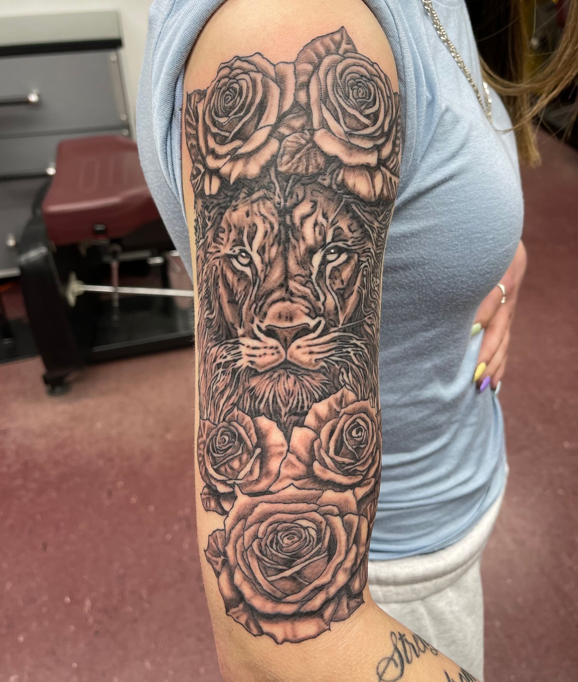 Arm tattoo with roses and a lion face on a person’s forearm in a indoor setting