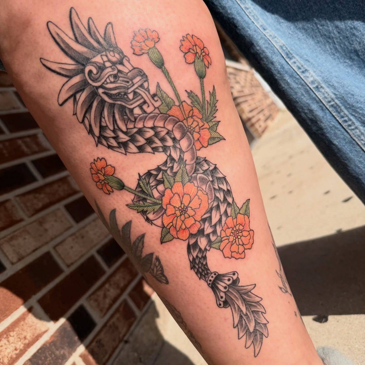 Arm tattoo of a black-and-gray dragon entwined with orange flowers and green leaves