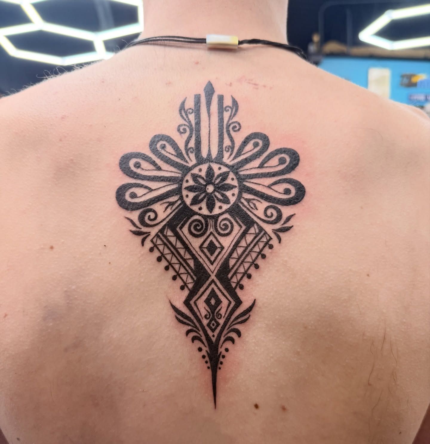 Black geometric tattoo centered on an upper back, with symmetrical floral and diamond patterns.