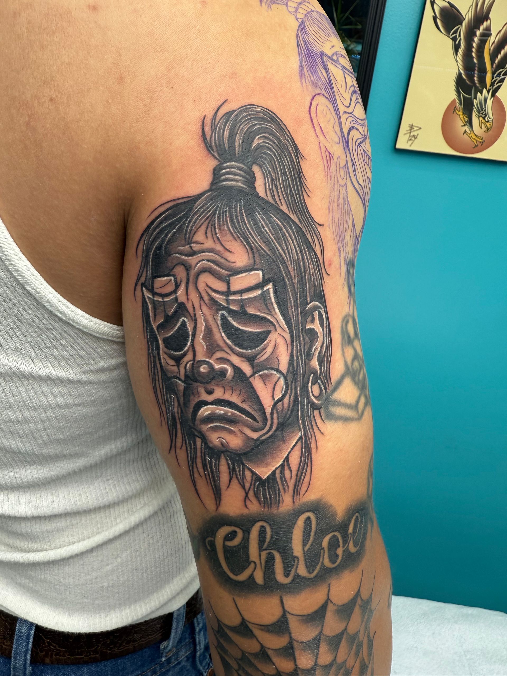 Arm tattoo portrait of a sorrowful face with the name “Chloe” beneath it