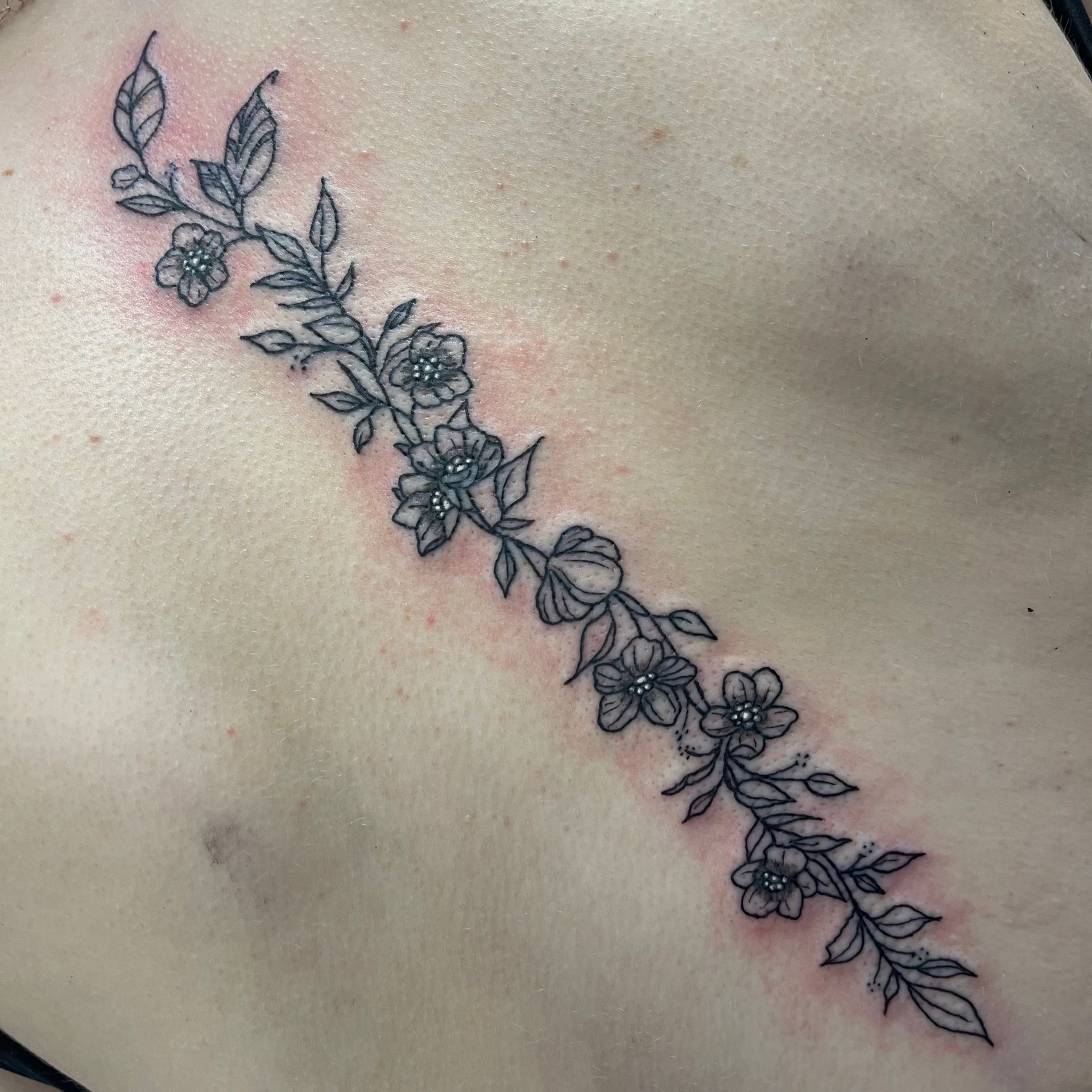 Floral vine tattoo with small black outlined flowers across a shoulder blade