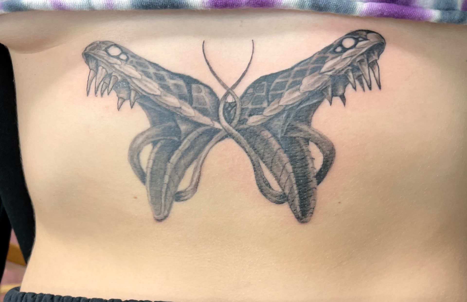 Black butterfly tattoo centered on a person’s lower back, with wings spread symmetrically