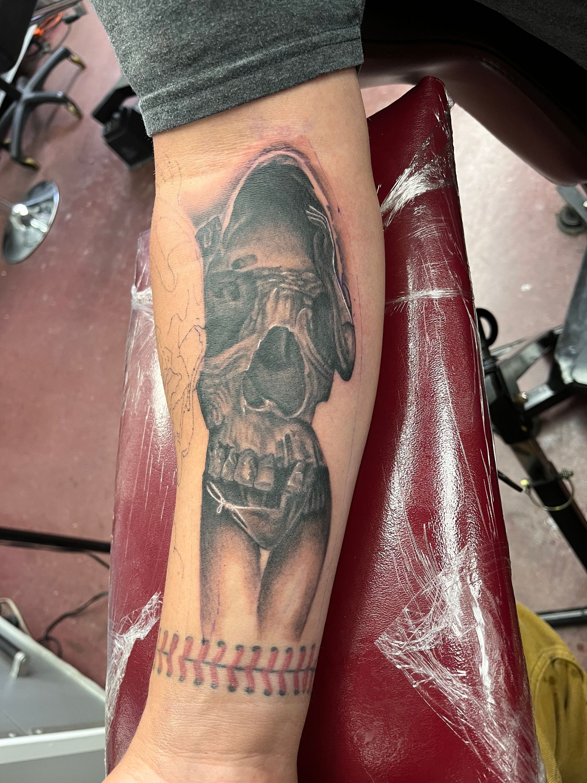 Close-up of a leg with a black tattoo, resting on a red salon chair covered in protective wrap