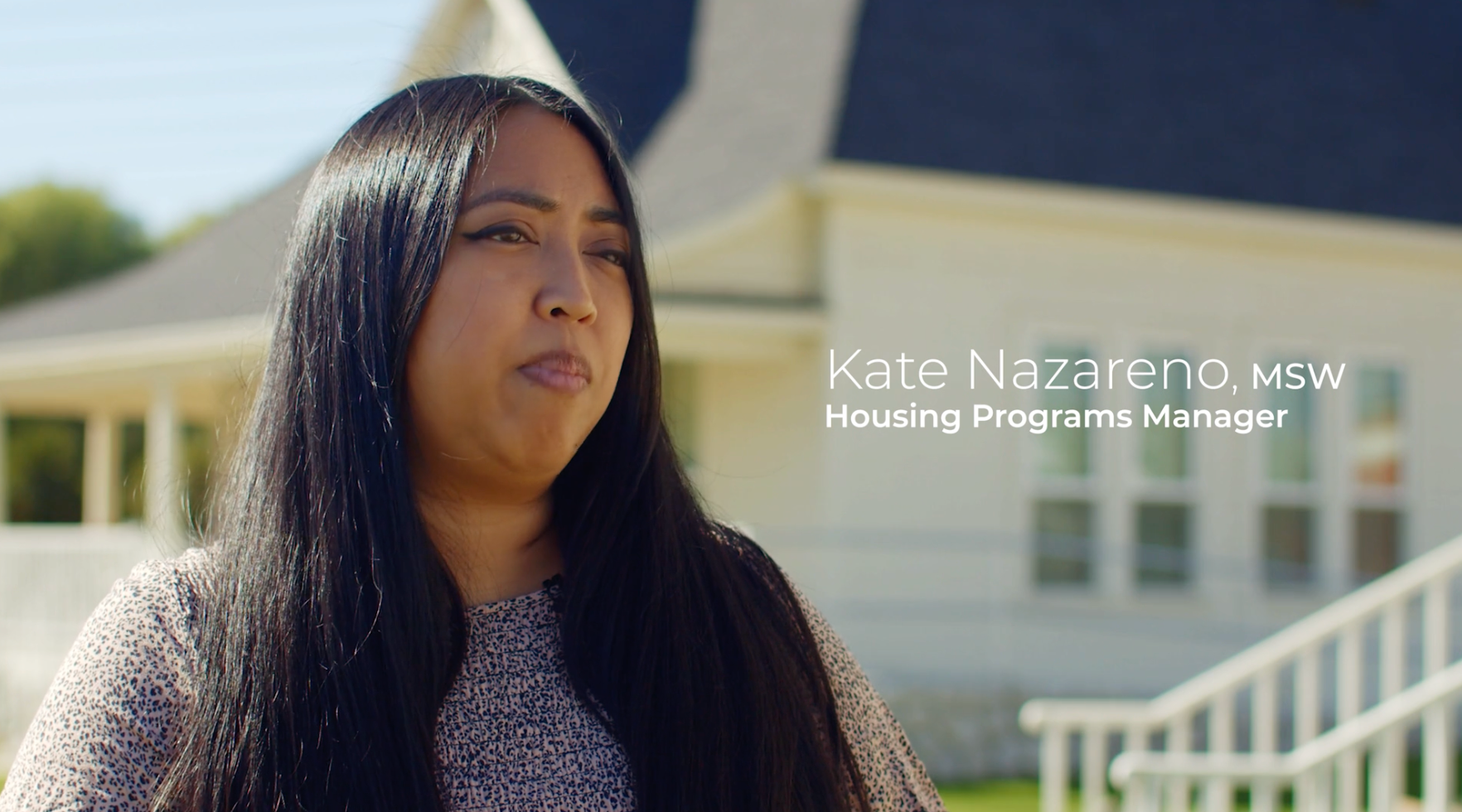 Woman speaking in front of a house; text reads 