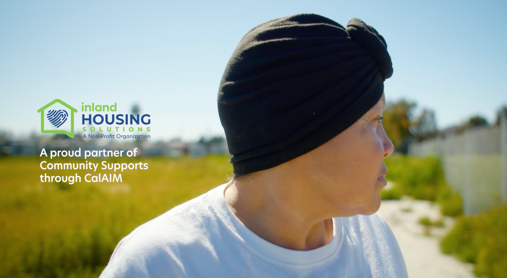 Person in black head covering, looking right, outdoors. Inland Housing Solutions logo visible.