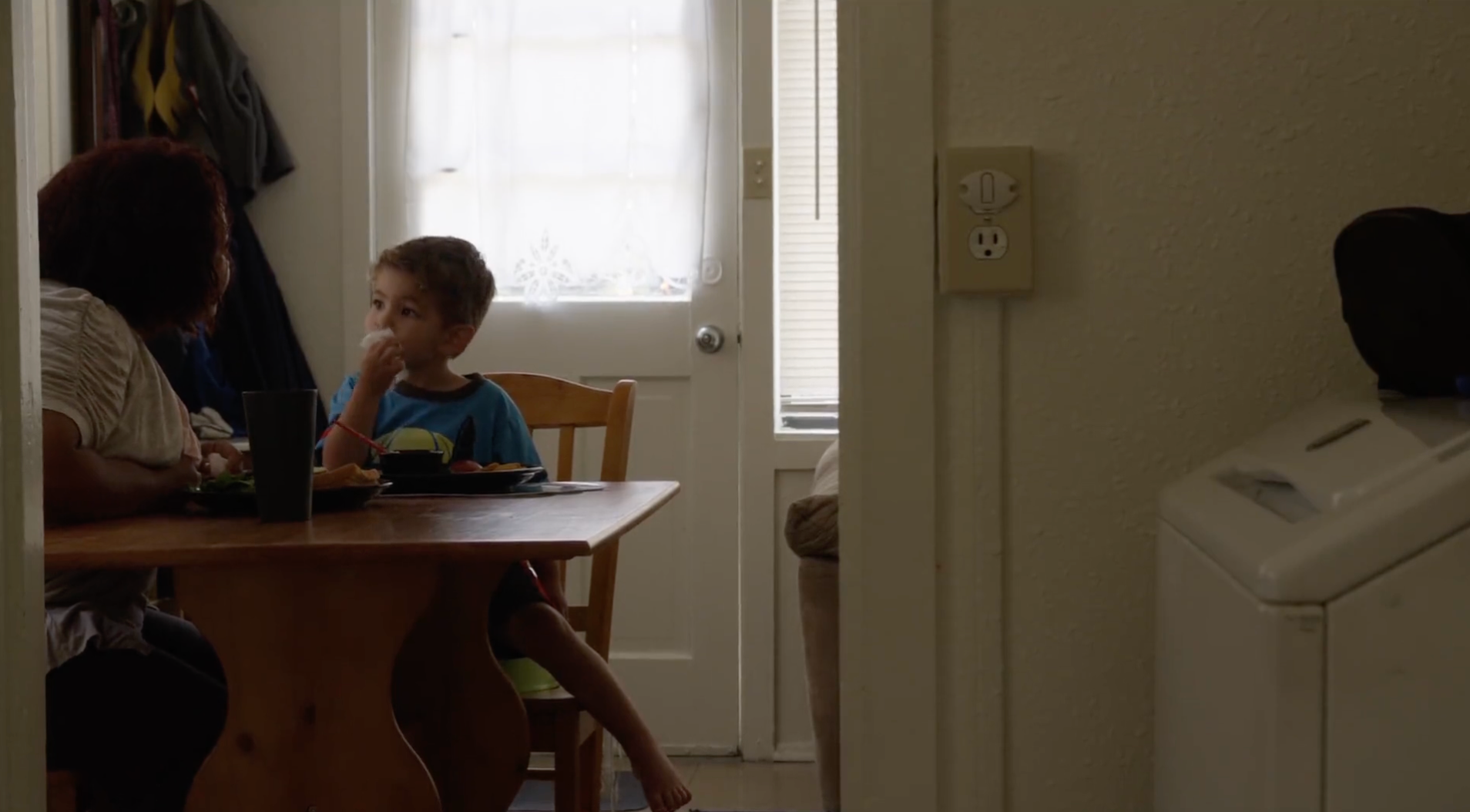 Woman and young boy seated at a wooden table in a kitchen, eating.