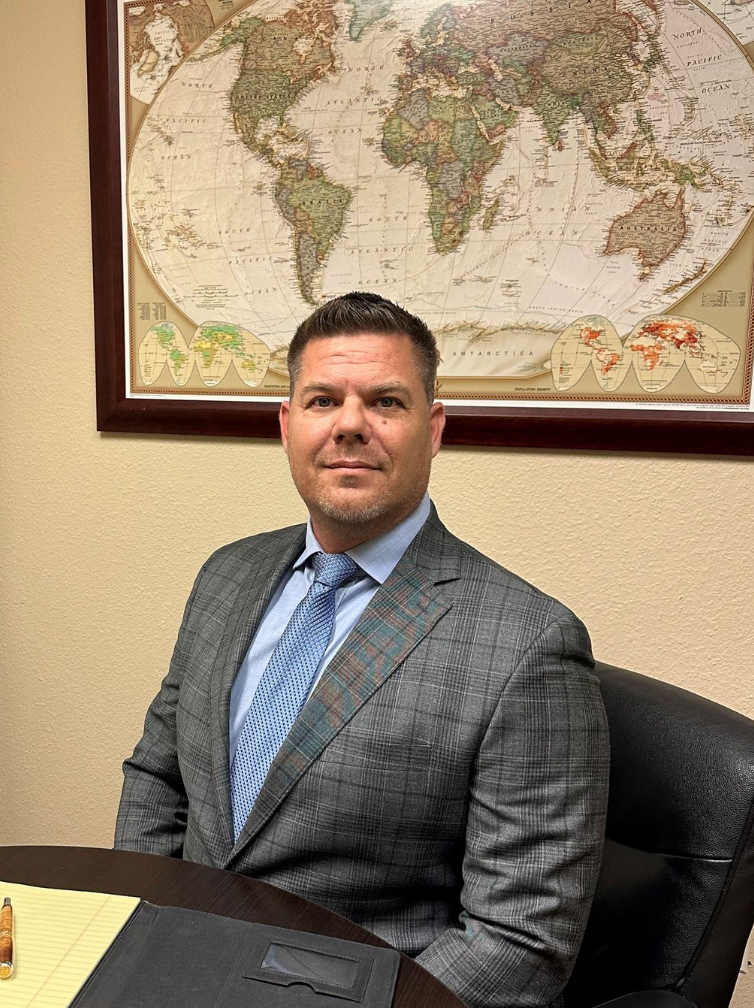 A man in a suit and tie is sitting at a table in front of a map of the world.