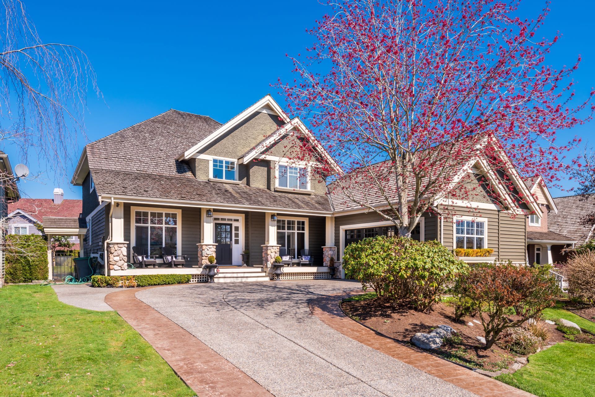 Suburban house with stone facade, front porch, driveway, and blooming pink tree in spring