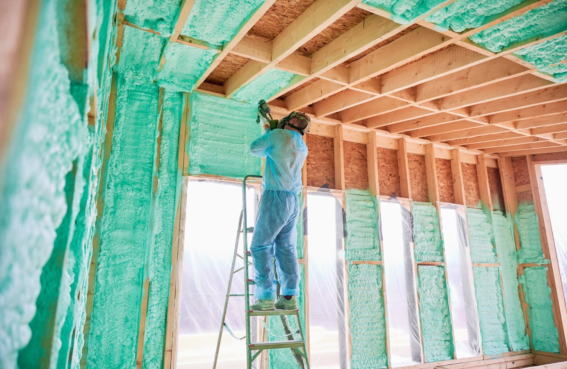 Worker spray-foaming insulation on exposed wall and ceiling framing in a house under construction