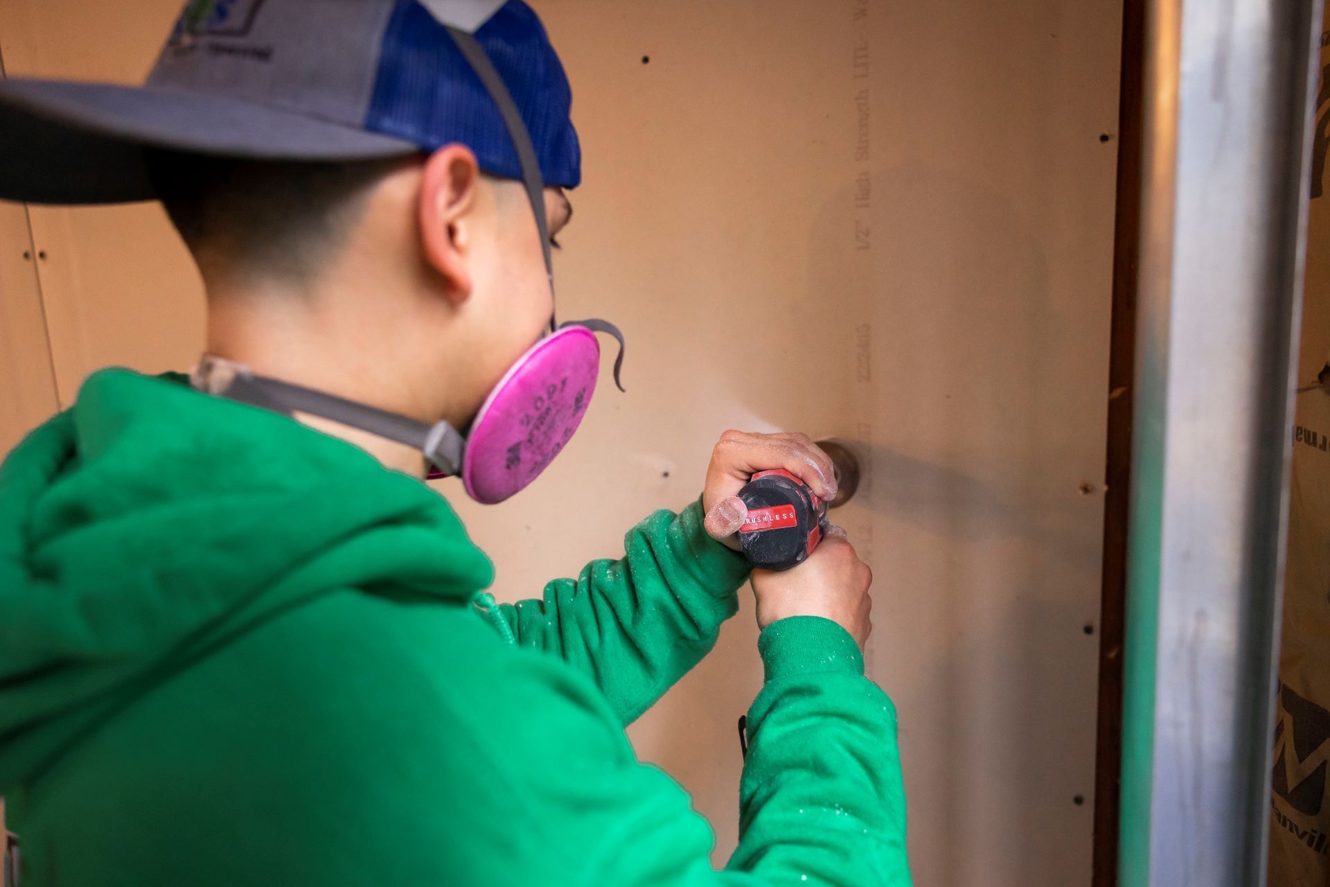 A man wearing a mask is using a drill to drill a hole in a wall.