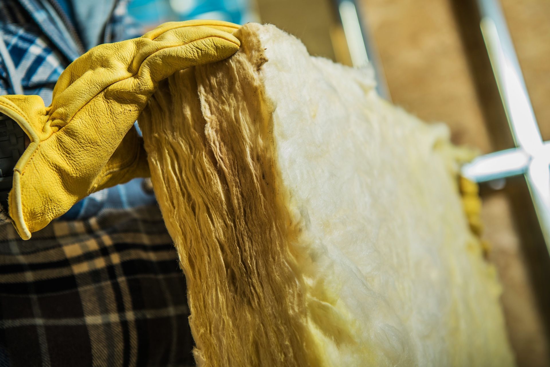 Person wearing yellow gloves holding a fiberglass insulation panel.