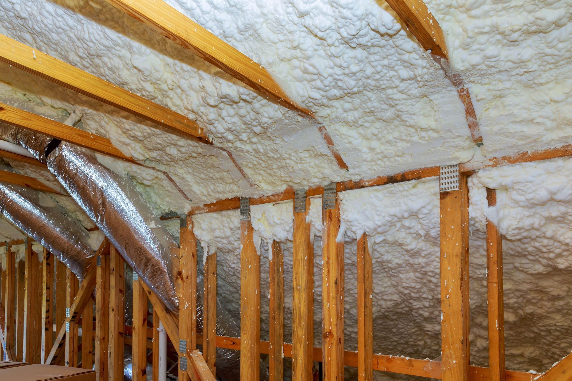 Spray foam insulation applied to the underside of a wooden roof deck and wall studs in an unfinished attic.
