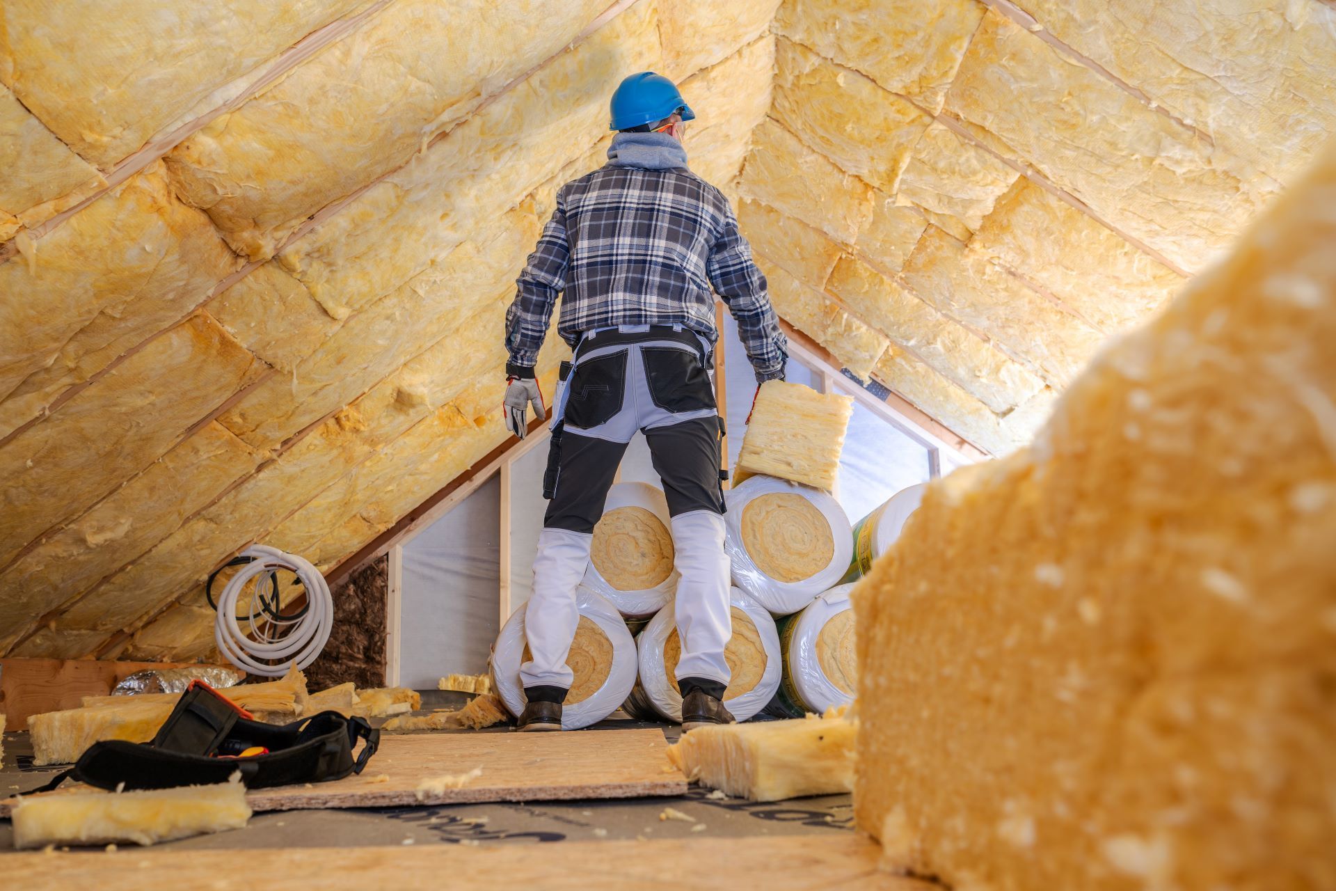 Worker in blue hard hat installing insulation inside an attic with yellow foam panels.