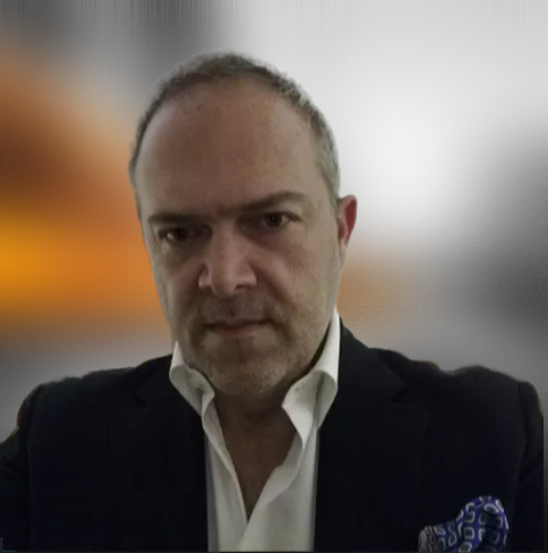 A man in a black blazer and white dress shirt with a patterned pocket square, looking directly at the camera.