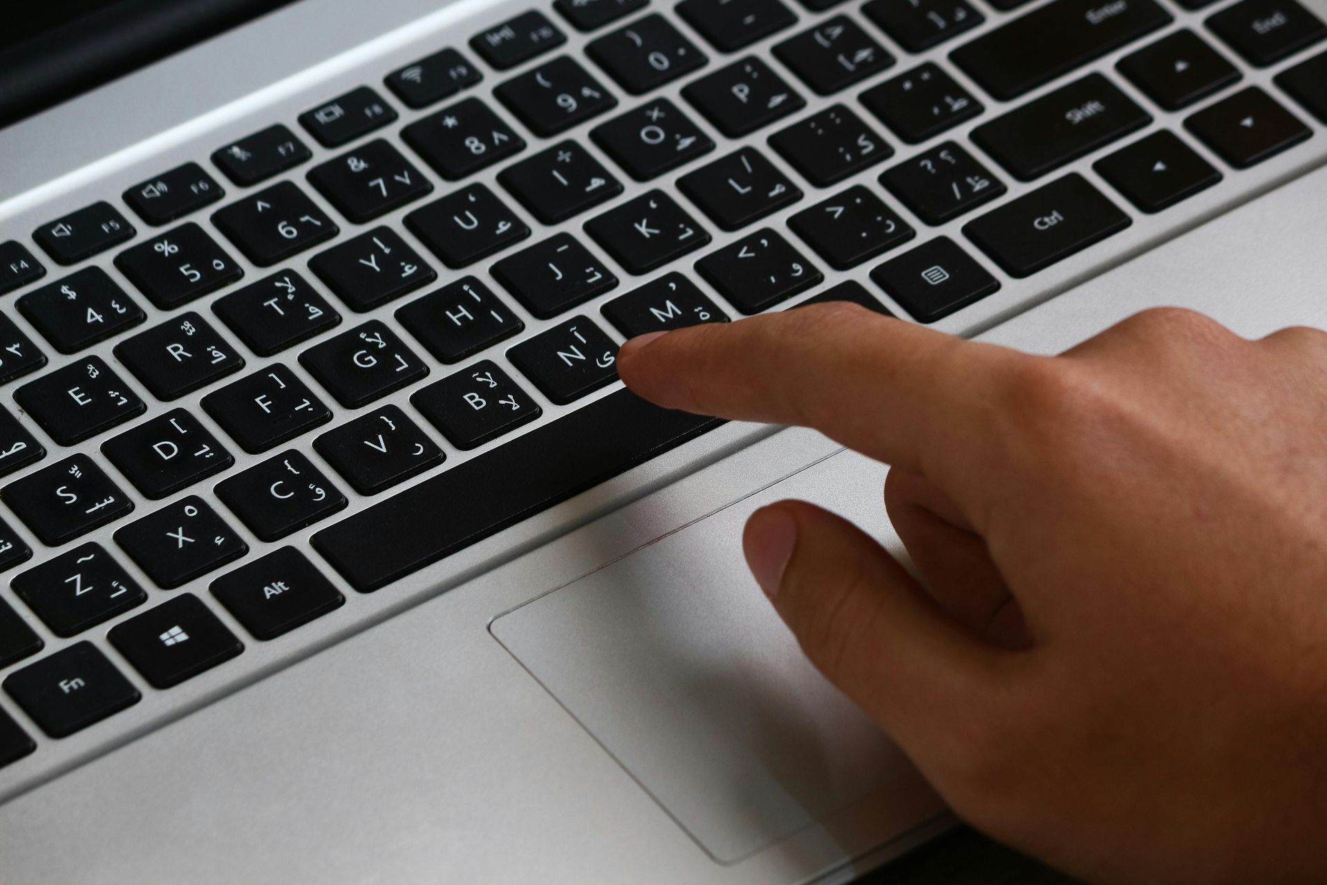 A hand rests on a laptop keyboard with bilingual keys, positioned over the trackpad.