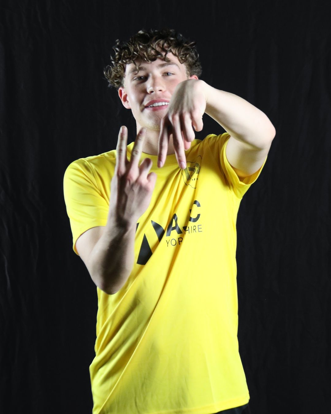 Young person in yellow shirt gesturing with hands; black background.