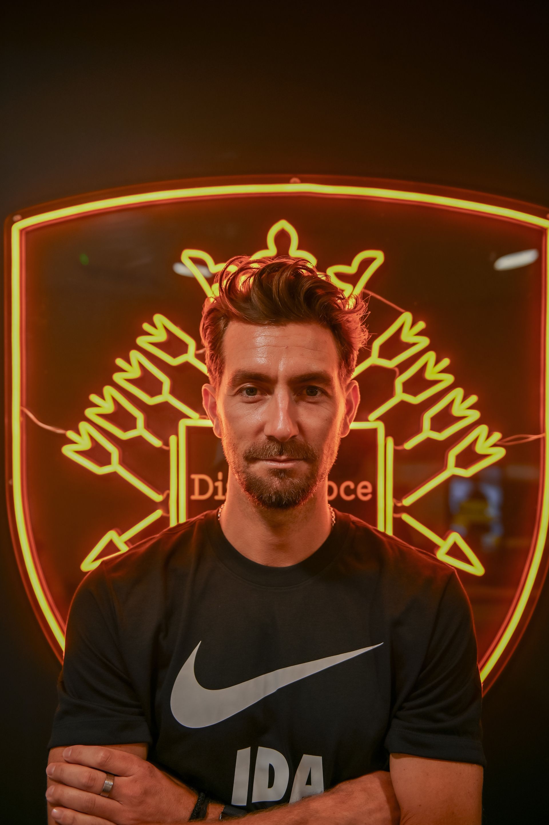 Man in black shirt with Nike logo in front of a neon illuminated crest.