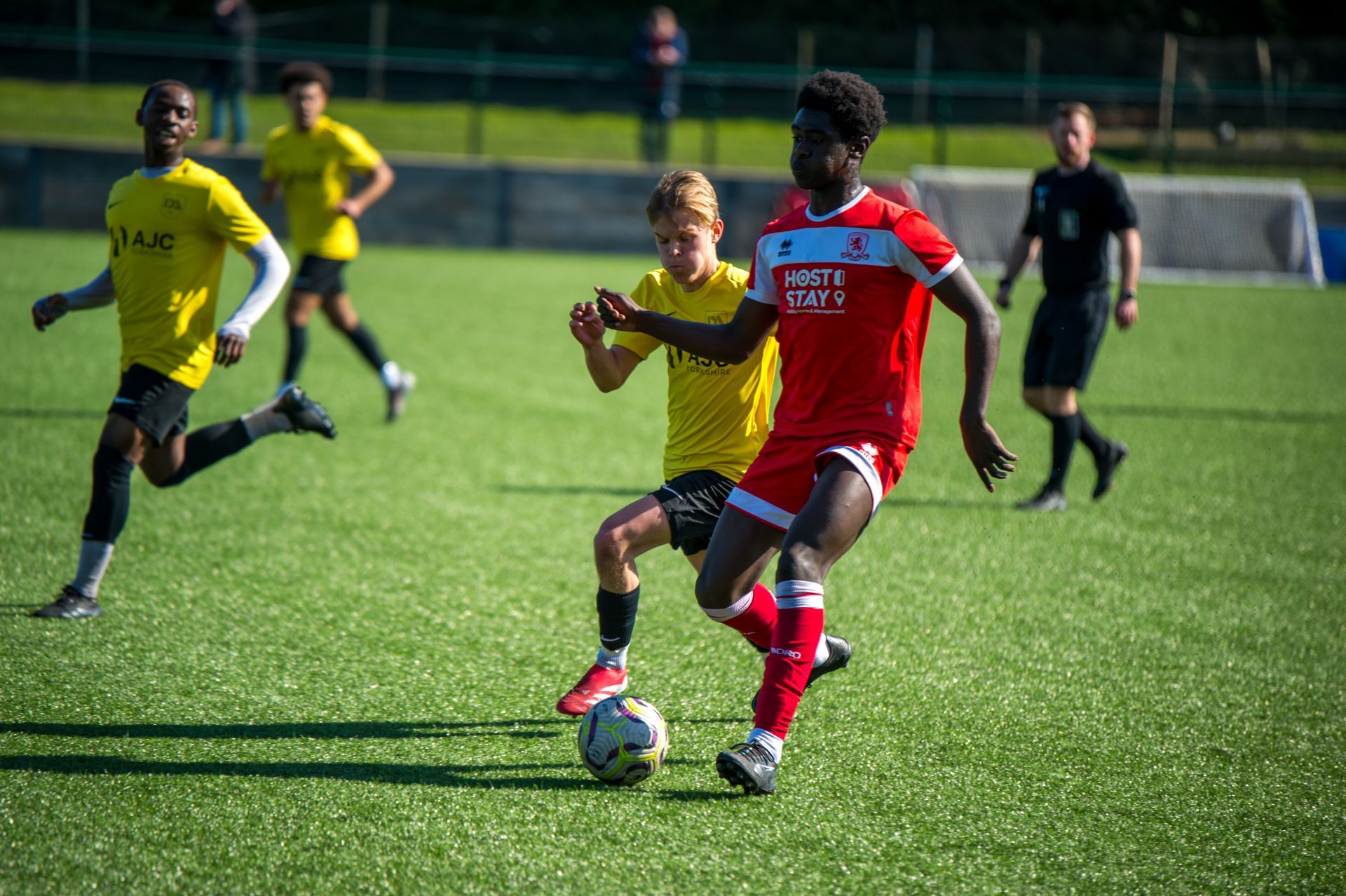 Soccer players in action on green field. Red-shirted player dribbles ball, yellow-shirted player defends.