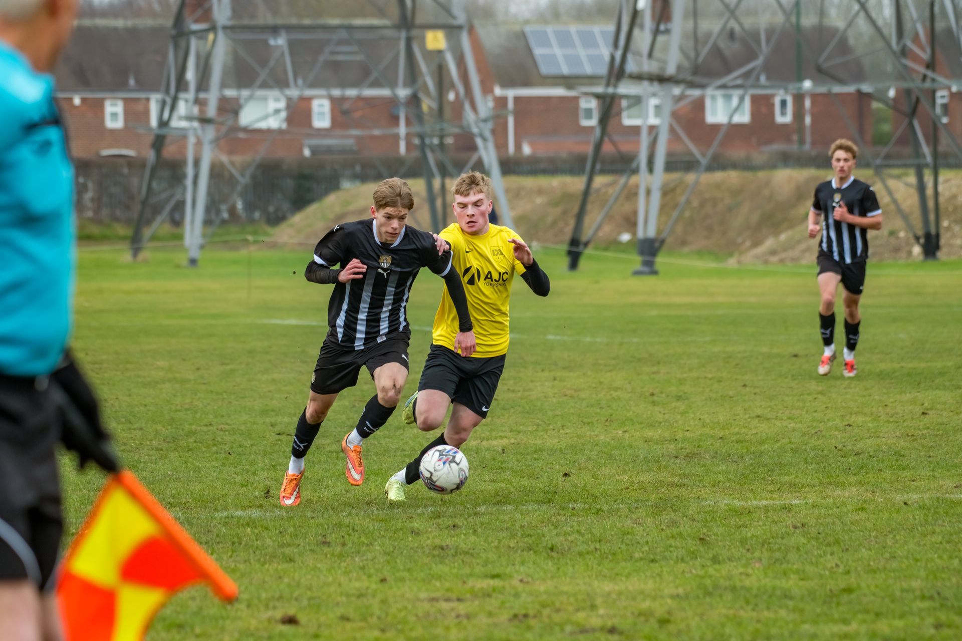 Two soccer players, one in yellow, one in black and white, chasing the ball on a grassy field.