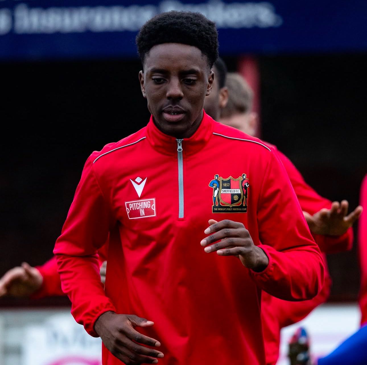 Soccer player in red training gear, on a field, looking forward, sleeves rolled up.