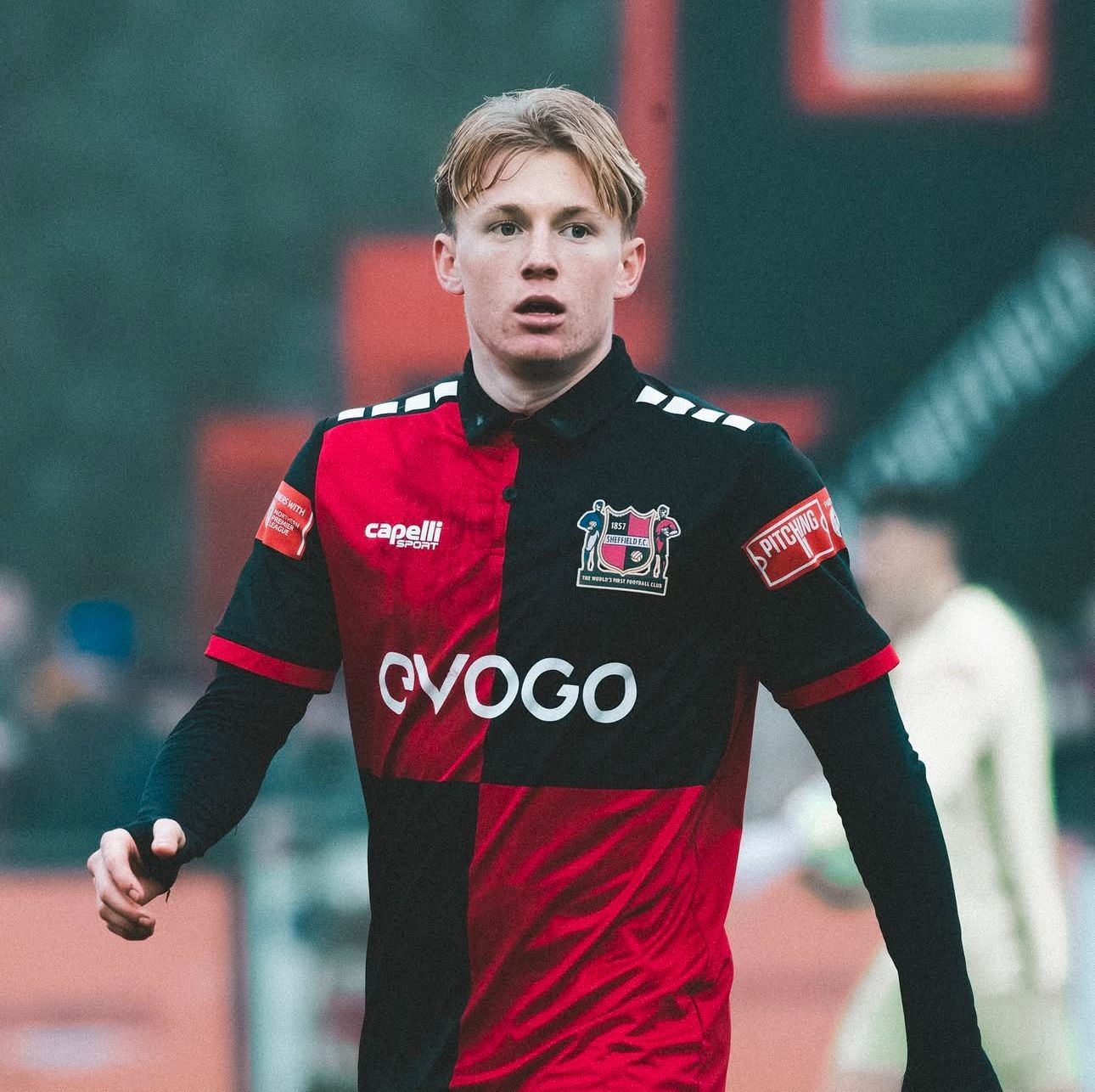 Soccer player in black and red uniform, looking forward on field.