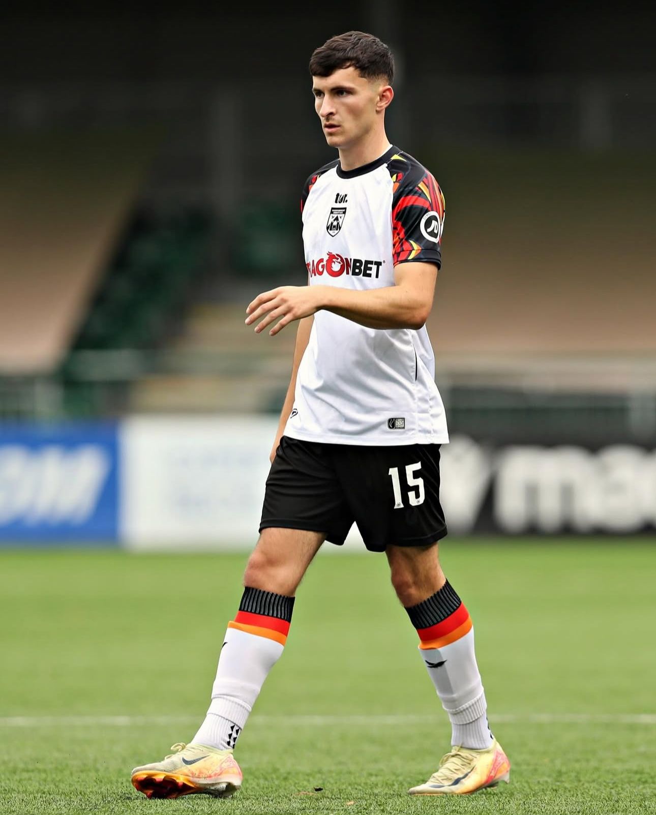 Soccer player in white jersey with black shorts, walking on a green field. Number 15 on shorts.