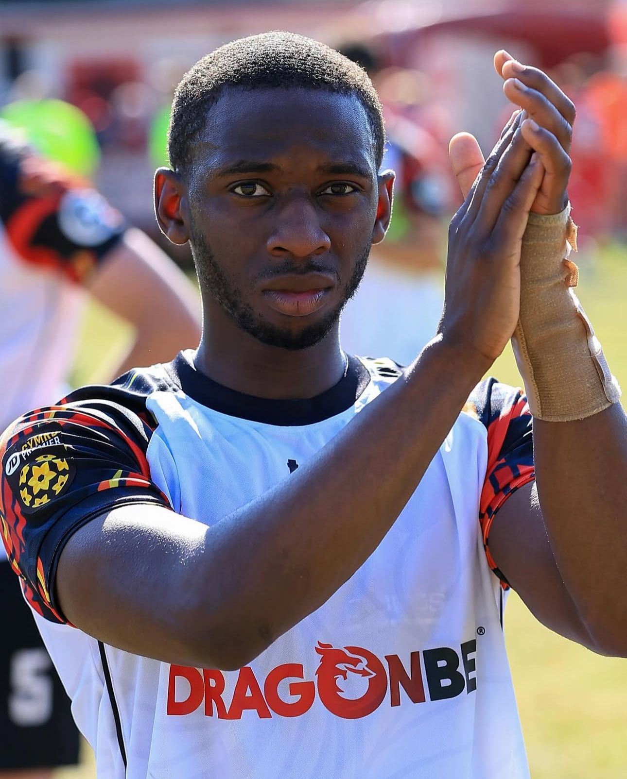 Soccer player in white jersey clapping; bandaged wrist.