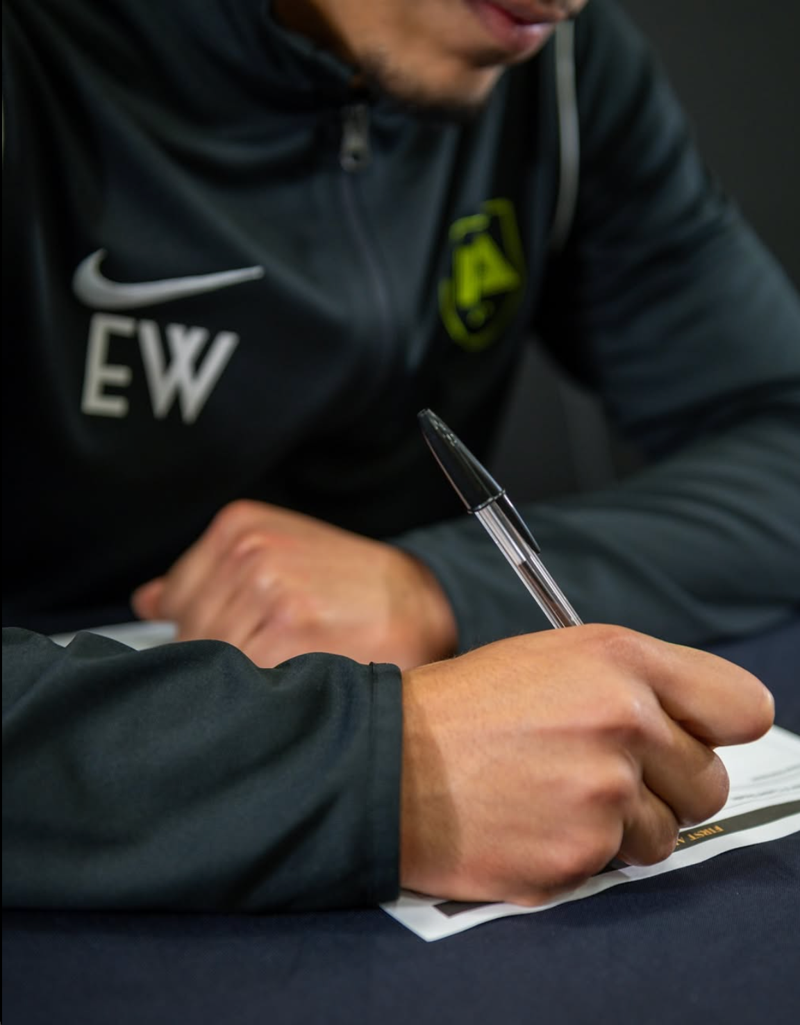 Person writing with a pen on a paper, wearing a black jacket with