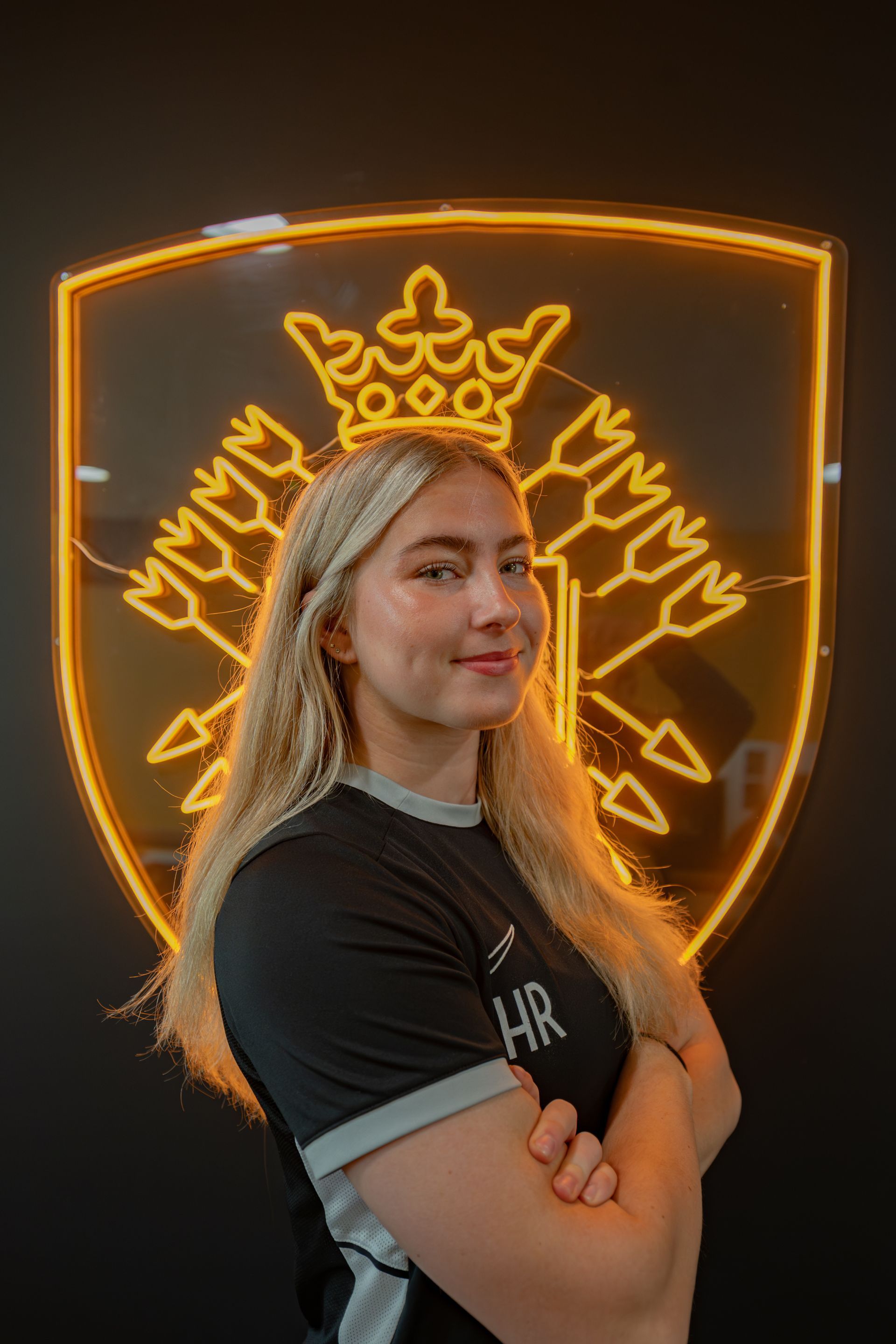 Woman with blonde hair, arms crossed, smiles. Black shirt with