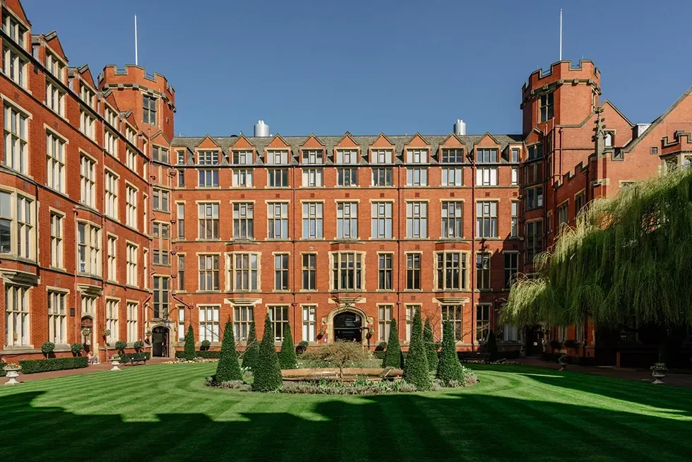Red brick university courtyard with green lawn and trimmed hedges.