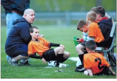 Soccer coach briefing young players in orange jerseys on a grassy field