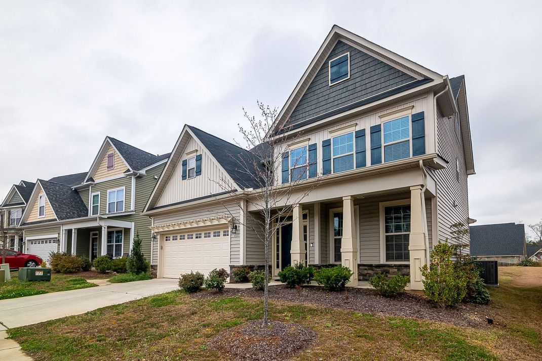 Suburban row of modern houses with garages, peaked roofs, and small front lawns under a cloudy sky