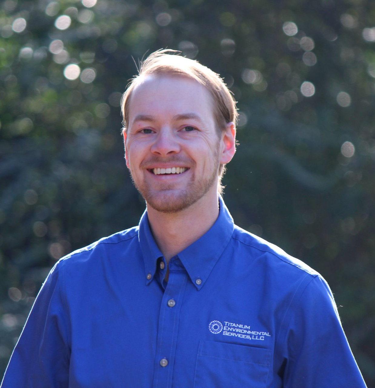 Man in blue shirt smiles outdoors.