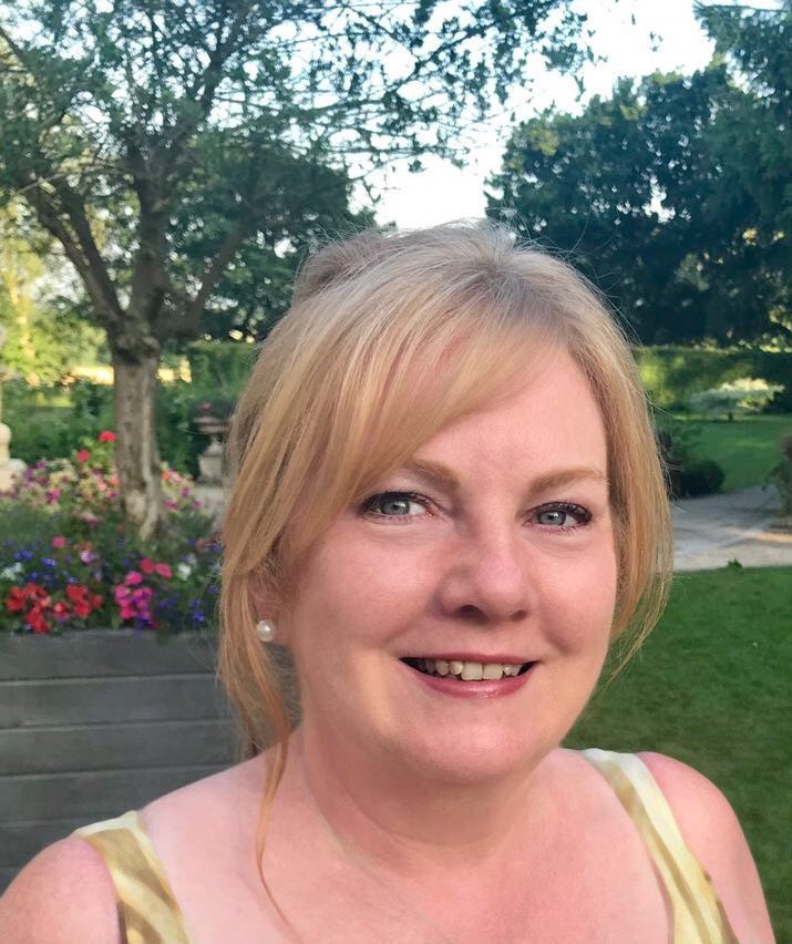 a woman with blonde hair is smiling in front of trees and flowers 
