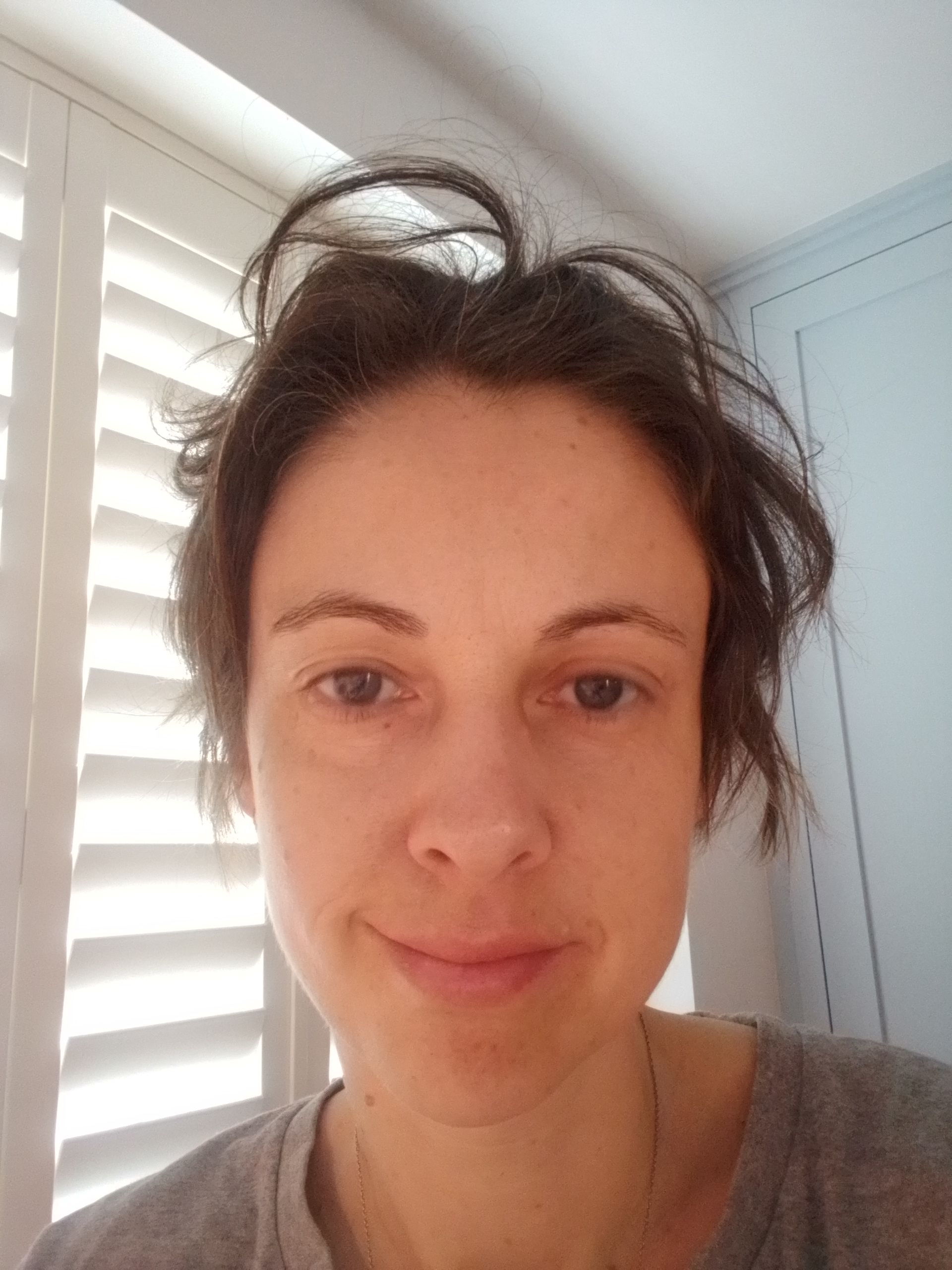 a woman with messy hair is taking a selfie in front of a window .
